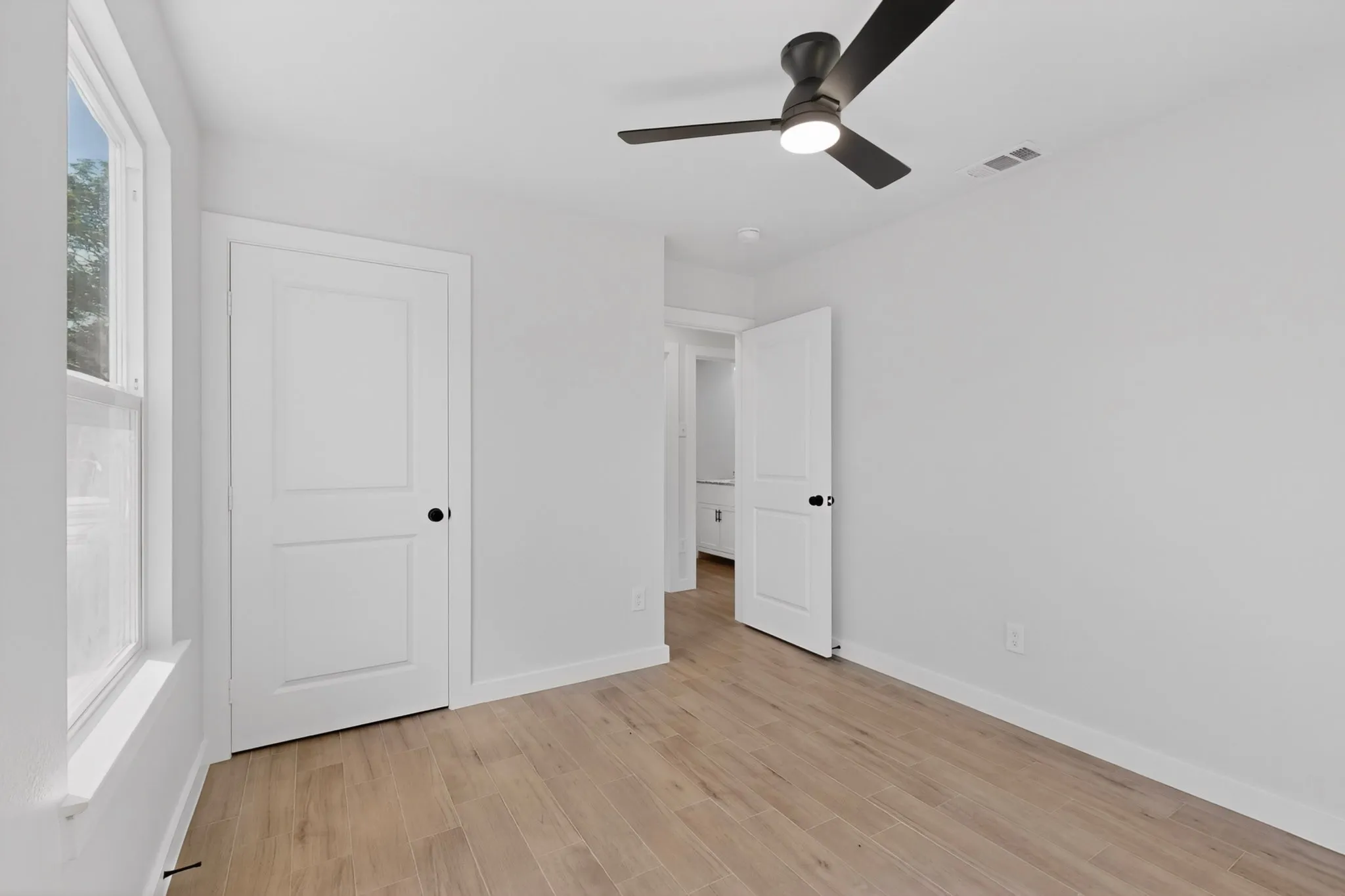 Bright interior room featuring wood-finish flooring, a contemporary ceiling fan with integrated lighting, and a white two-panel door
