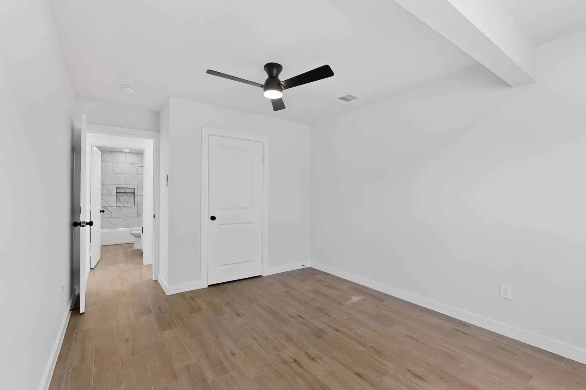 Room featuring wood-finish flooring, a contemporary ceiling fan with integrated lighting, and a white interior door with black hardware