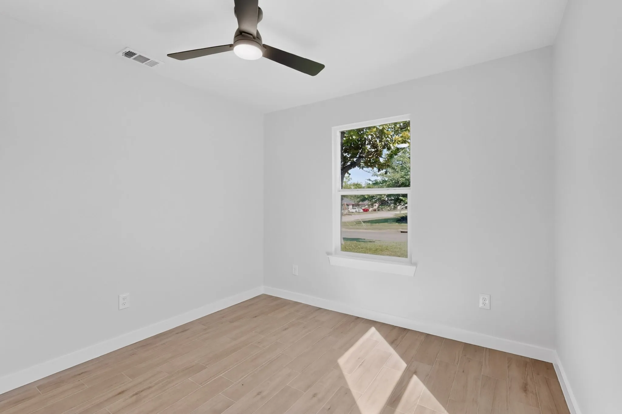 Light-filled room featuring wood-finish flooring and a contemporary ceiling fan