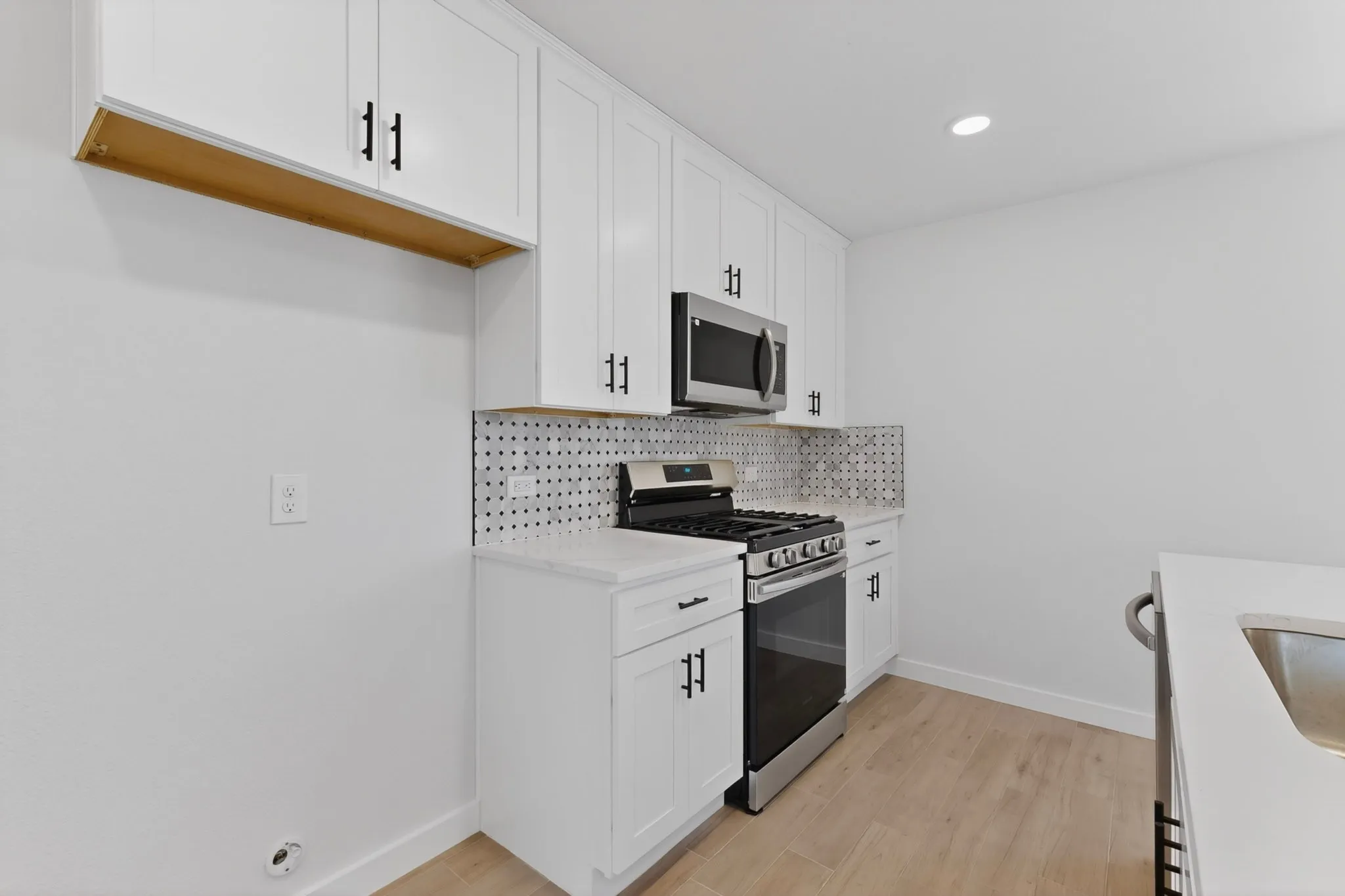 Kitchen featuring white shaker cabinetry with matte black hardware, stainless steel appliances, patterned tile backsplash, quartz countertops, and wood-finish flooring
