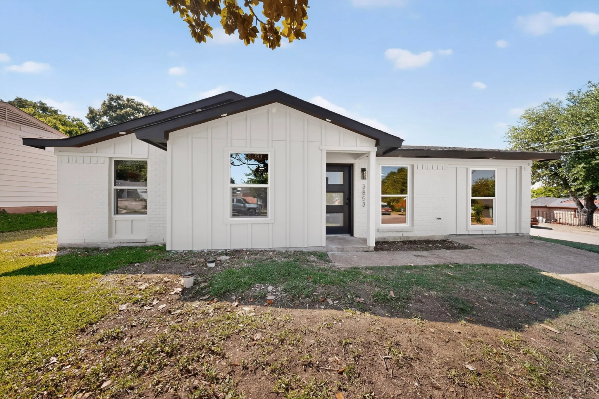 Modern exterior featuring white board and batten siding, white painted brick, a black roof, and a contemporary black entry door with frosted glass panels