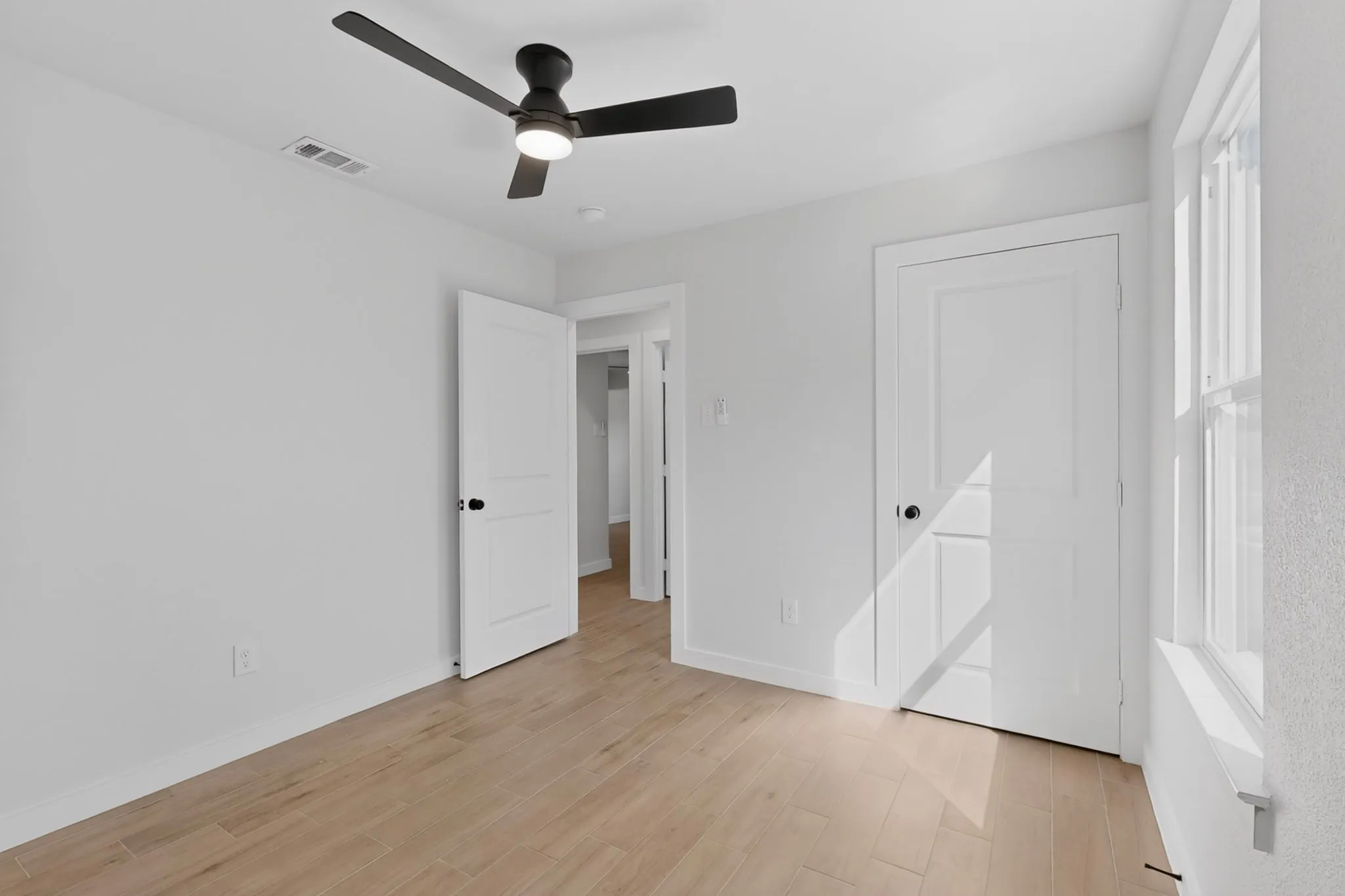 Interior room featuring wood-finish flooring, white walls, and a contemporary black ceiling fan with integrated lighting
