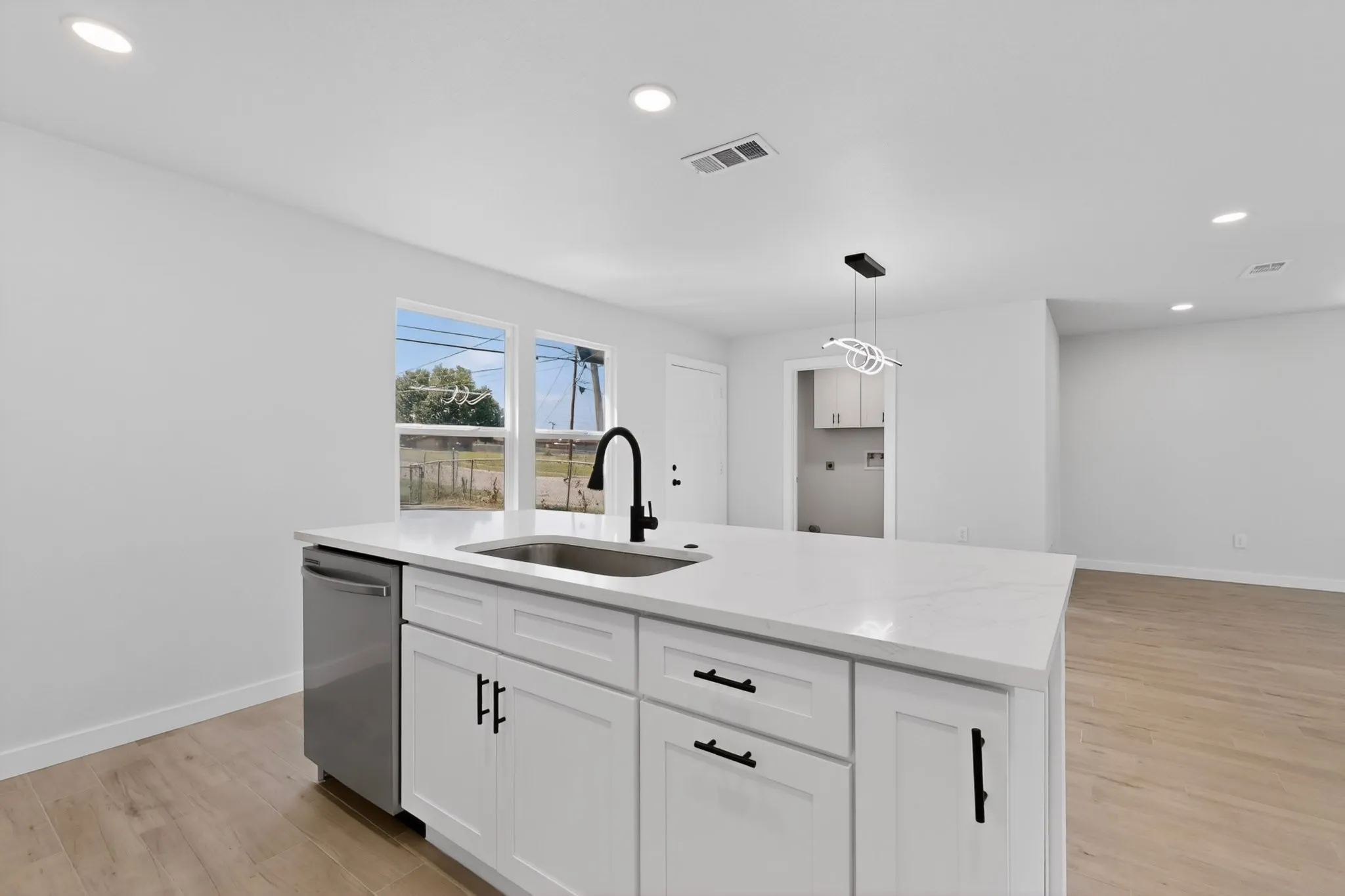 Kitchen island featuring a stainless steel sink with a black gooseneck faucet, white shaker-style cabinetry with black hardware, and a light-colored countertop