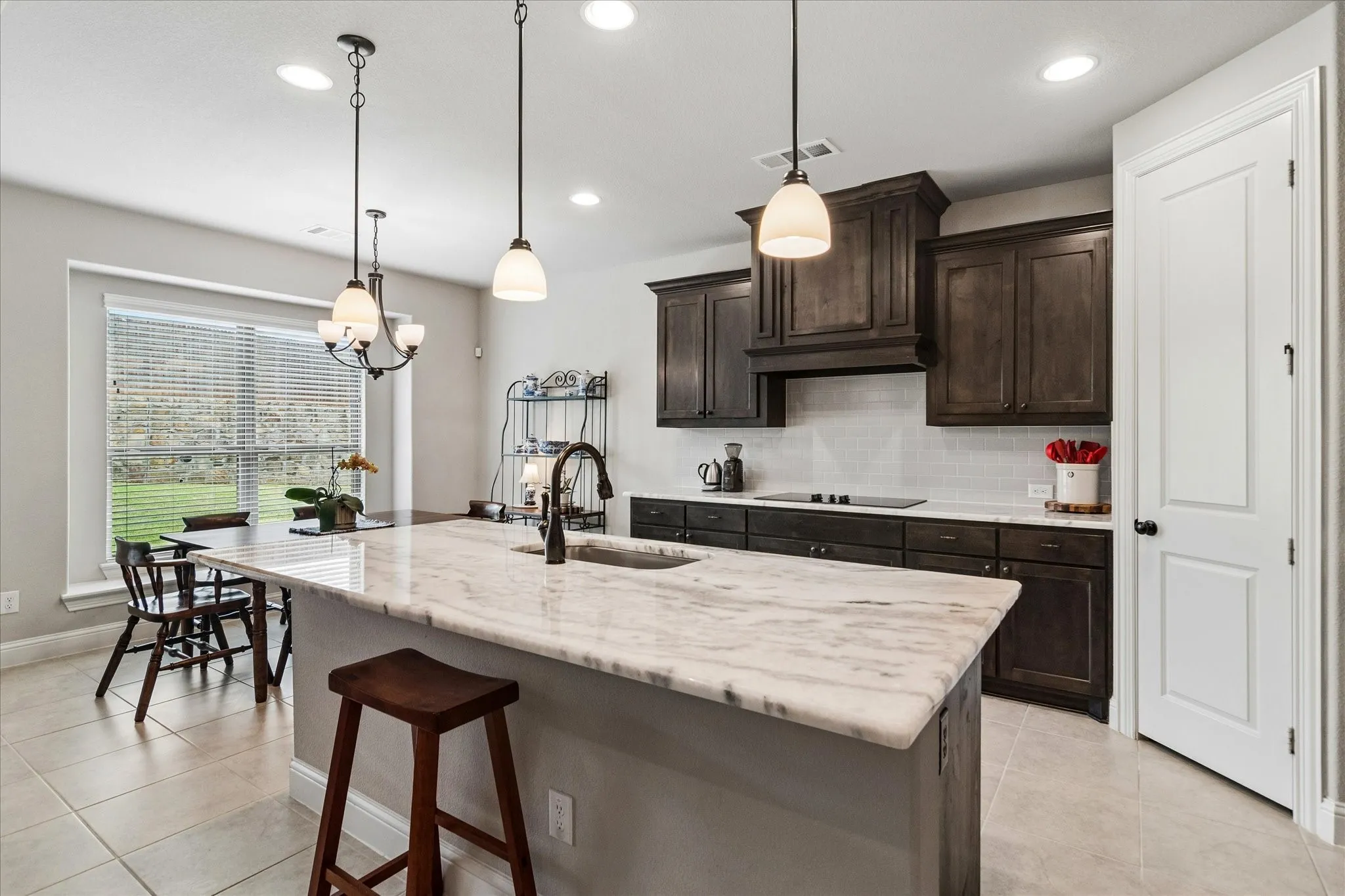 Kitchen featuring a large island with a substantial stone countertop, dark wood-finish cabinetry, a tile backsplash, tile flooring, and integrated ceiling lighting