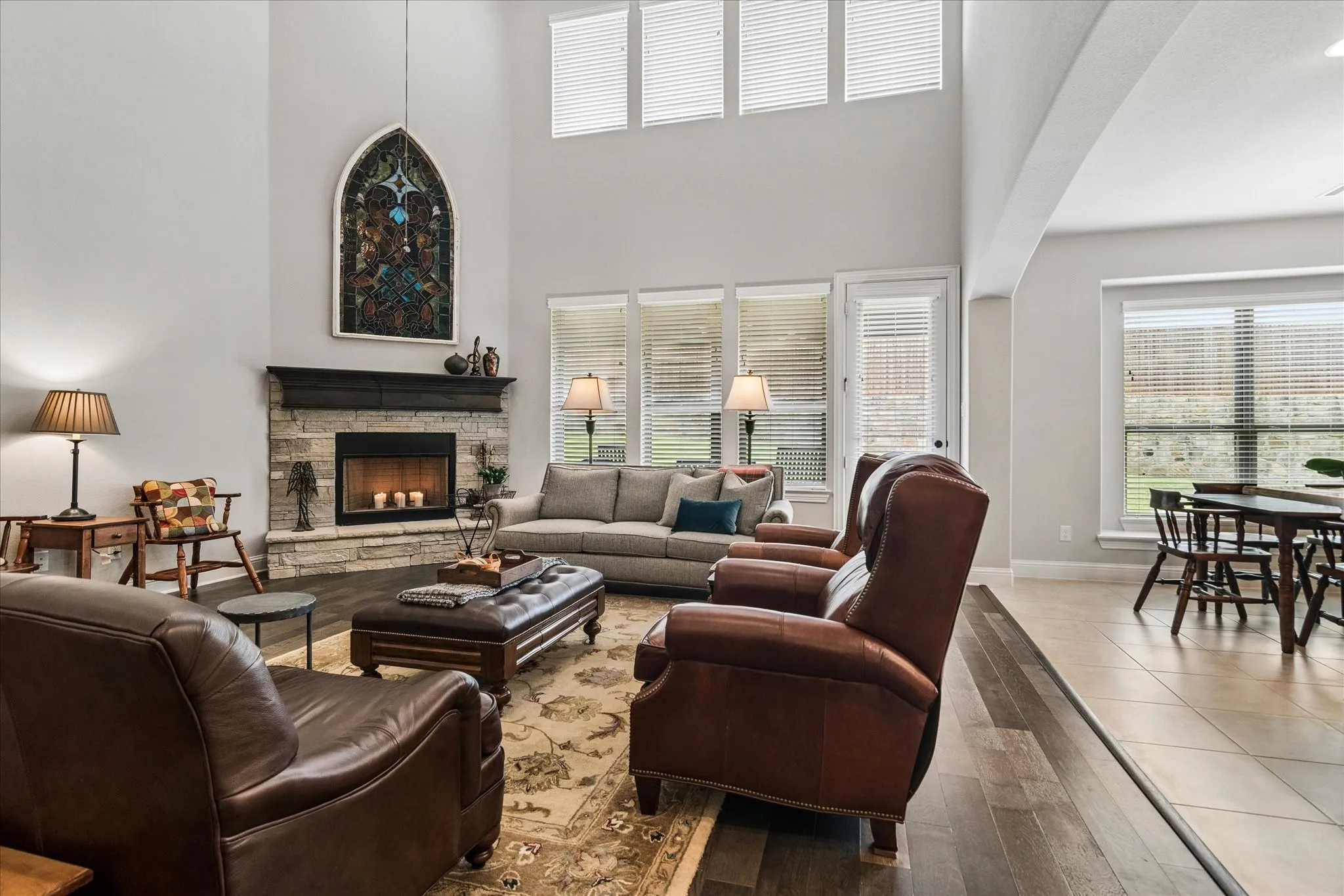 Vaulted living room with stone-faced fireplace, wood-finish flooring, and multiple windows