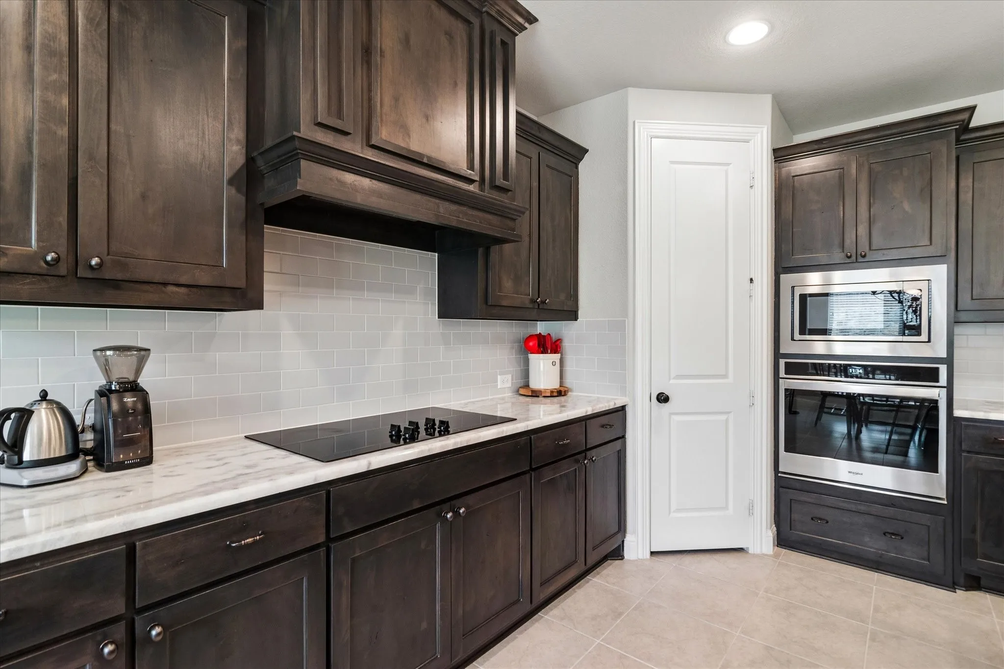 Kitchen featuring dark wood cabinetry, light-toned countertop, subway tile backsplash, and stainless steel built-in appliances including a wall oven and microwave