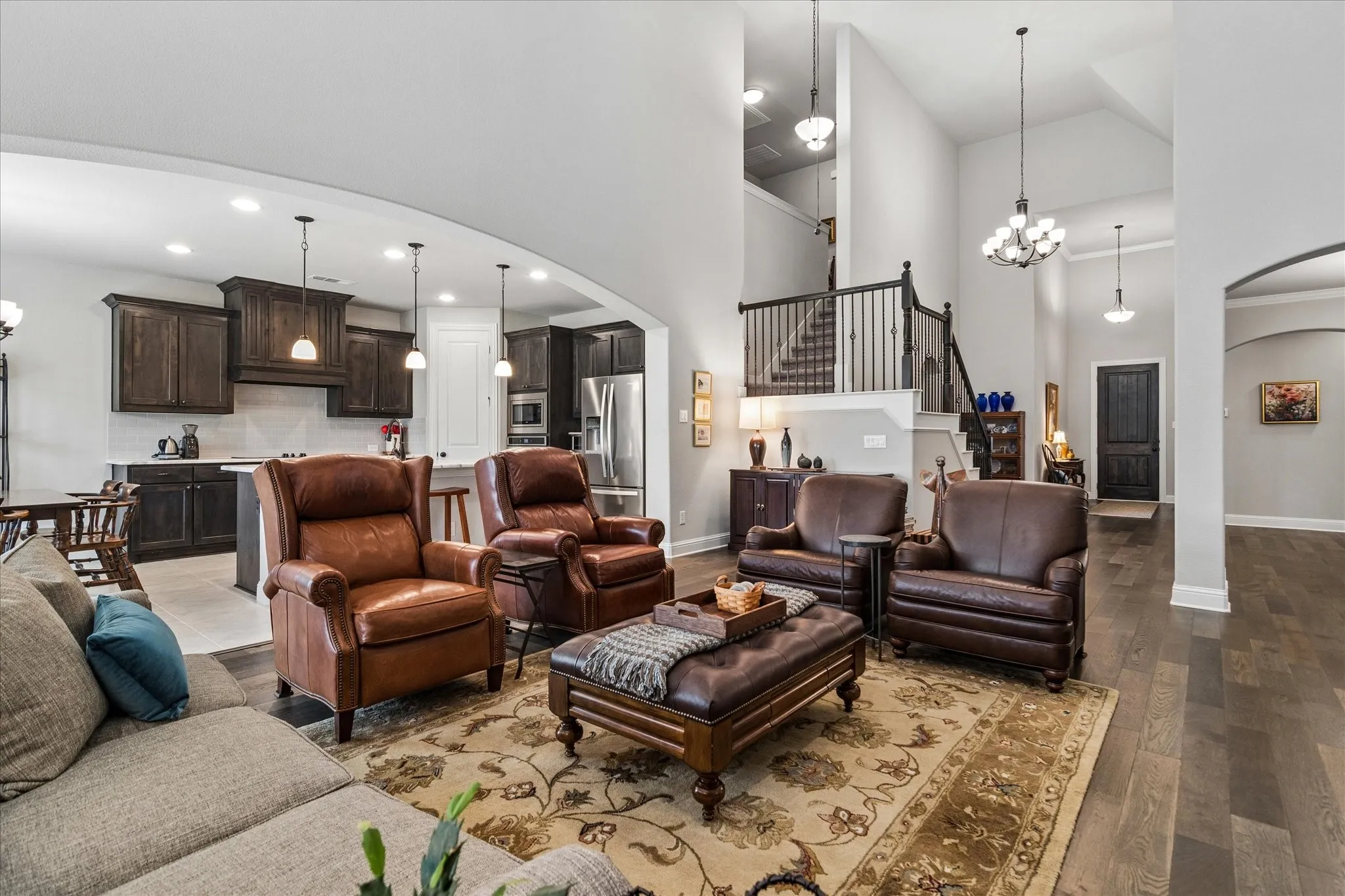 Open-concept living space featuring wood-finish flooring, a two-story ceiling, and a prominent staircase with dark wood railings and black iron balusters