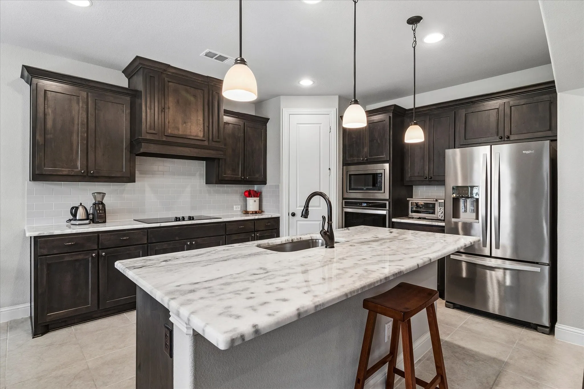 Kitchen featuring a stone-look island with an undermount sink and matte black faucet, dark wood cabinetry, stainless steel appliances, and pendant lighting