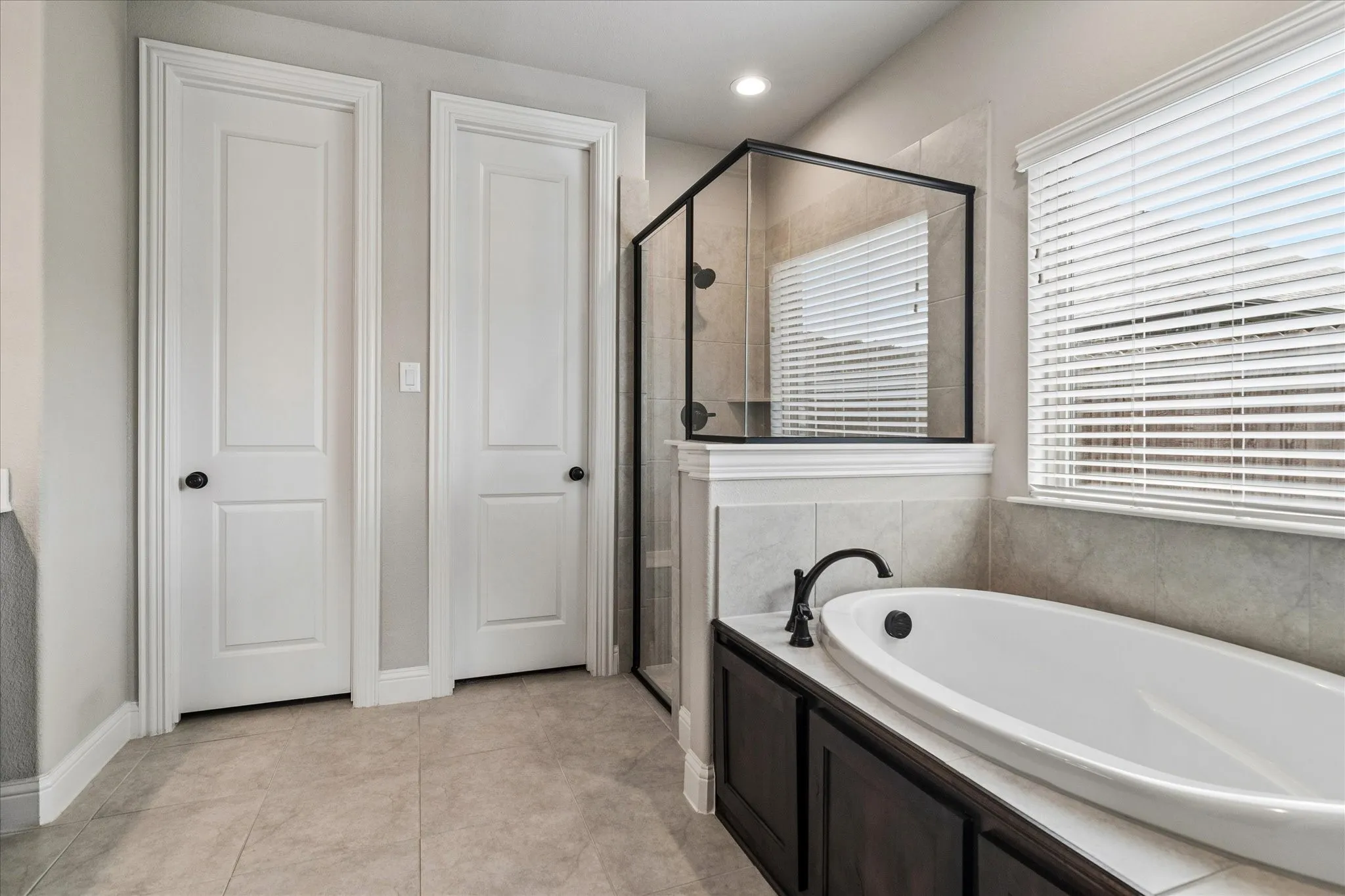 Soaking tub with a matte black faucet, surrounded by tiled walls, featuring an adjacent glass-enclosed shower with black trim