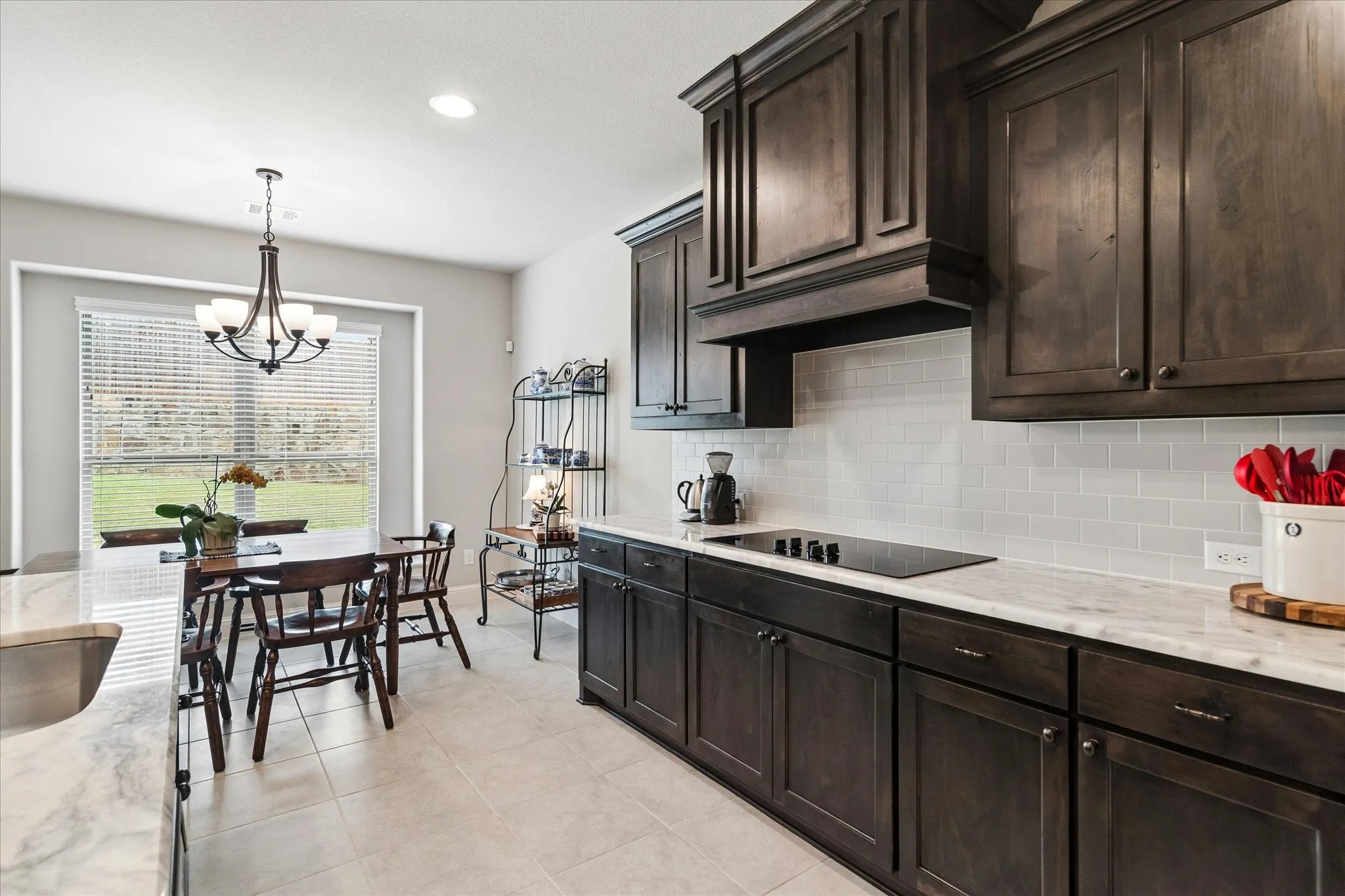Modern kitchen featuring dark wood cabinetry with crown molding, quartz countertops, a contemporary cooktop, and a subway tile backsplash