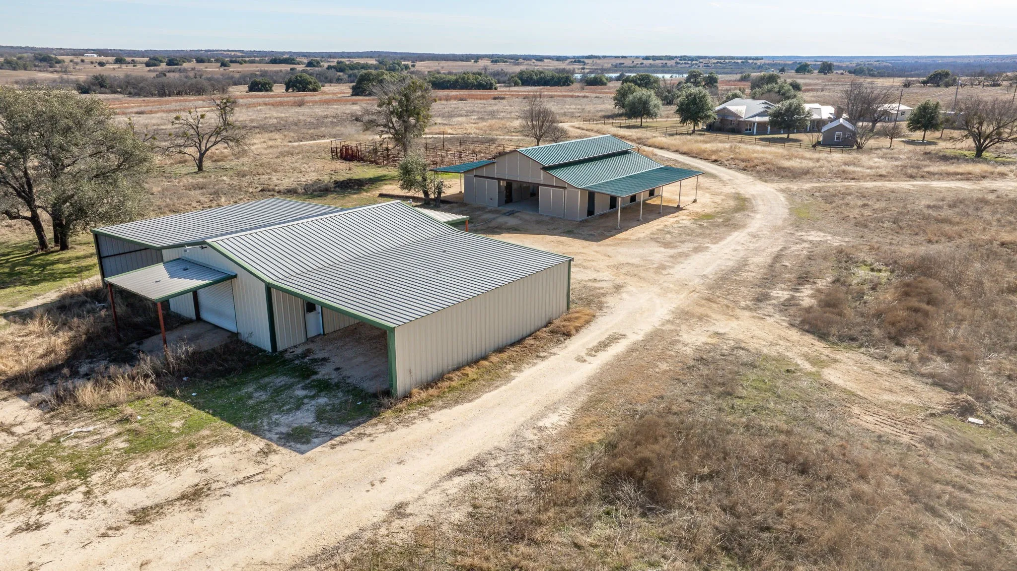 Multiple metal outbuildings with green trim and covered areas, surrounded by expansive natural terrain