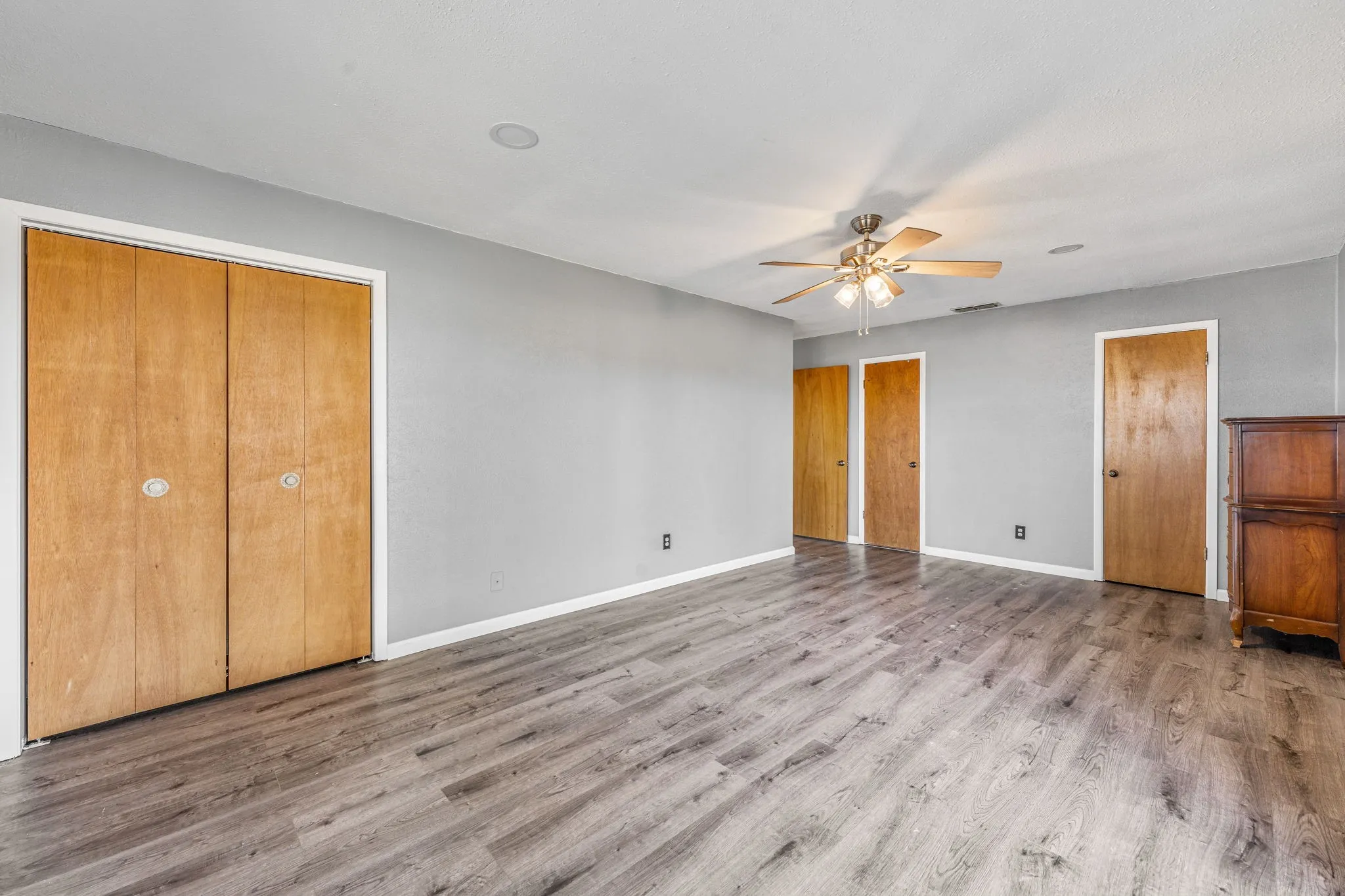 Spacious interior room featuring wood-finish flooring, light gray walls, and multiple solid wood doors