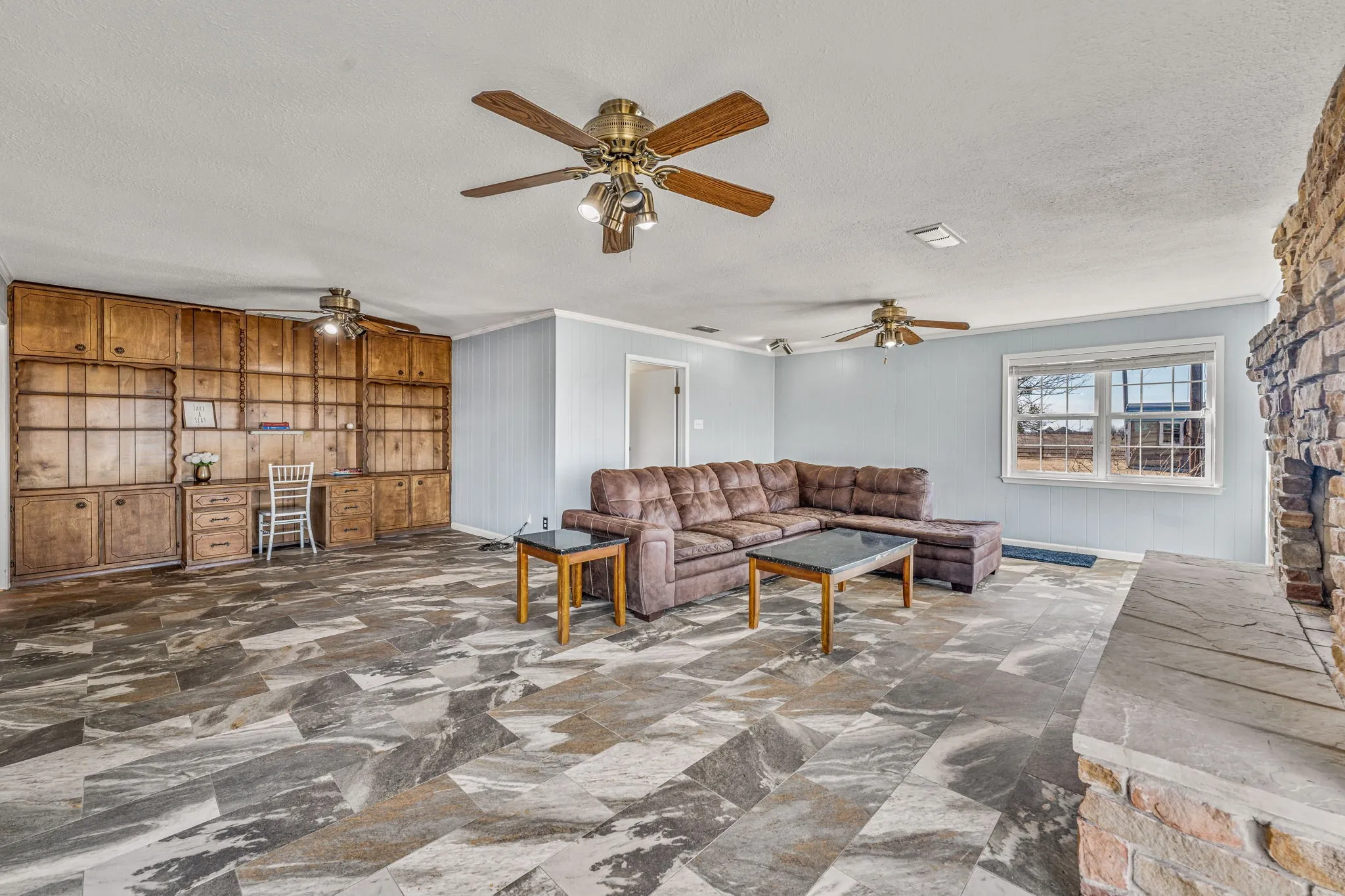Spacious interior featuring multi-toned tile flooring, light blue wall paneling, and a full-height stone fireplace with a substantial hearth