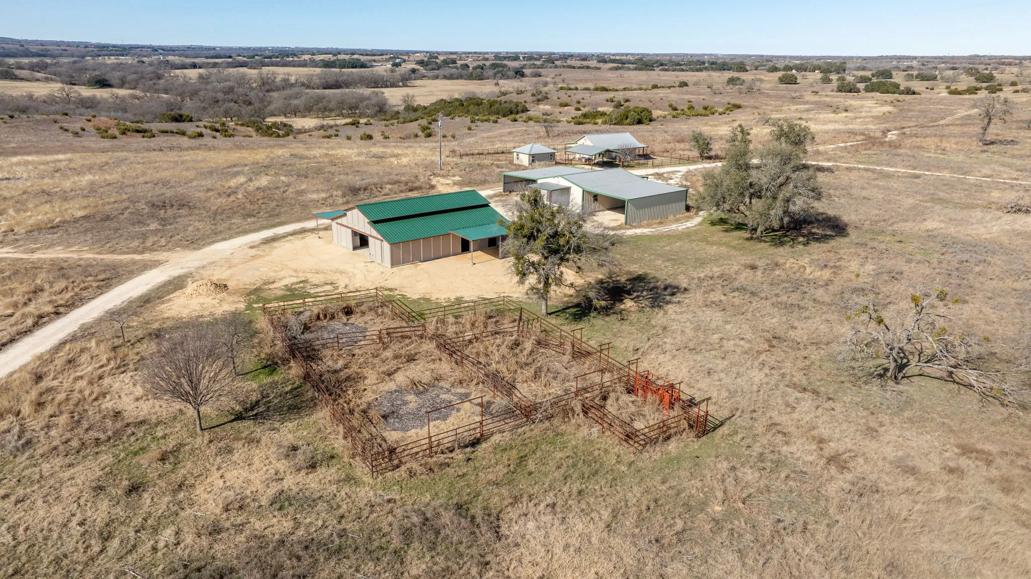 Ranch property featuring a barn with a green metal roof, multiple outbuildings, and fenced enclosures