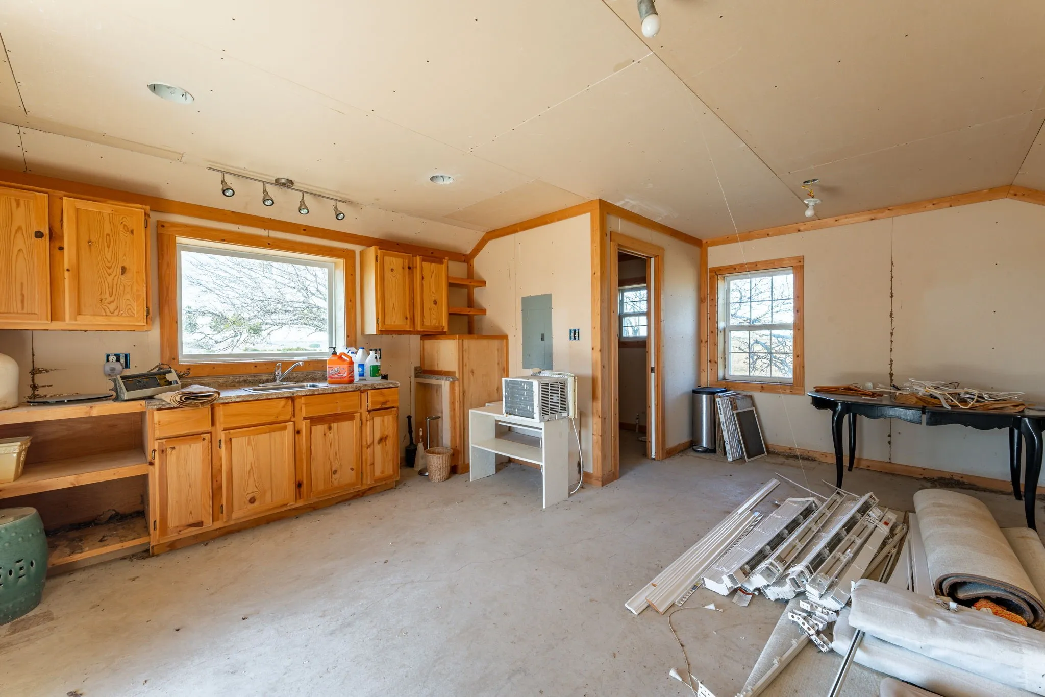 Open-concept room featuring light wood cabinetry with a sink, multiple windows, and wood-finish trim