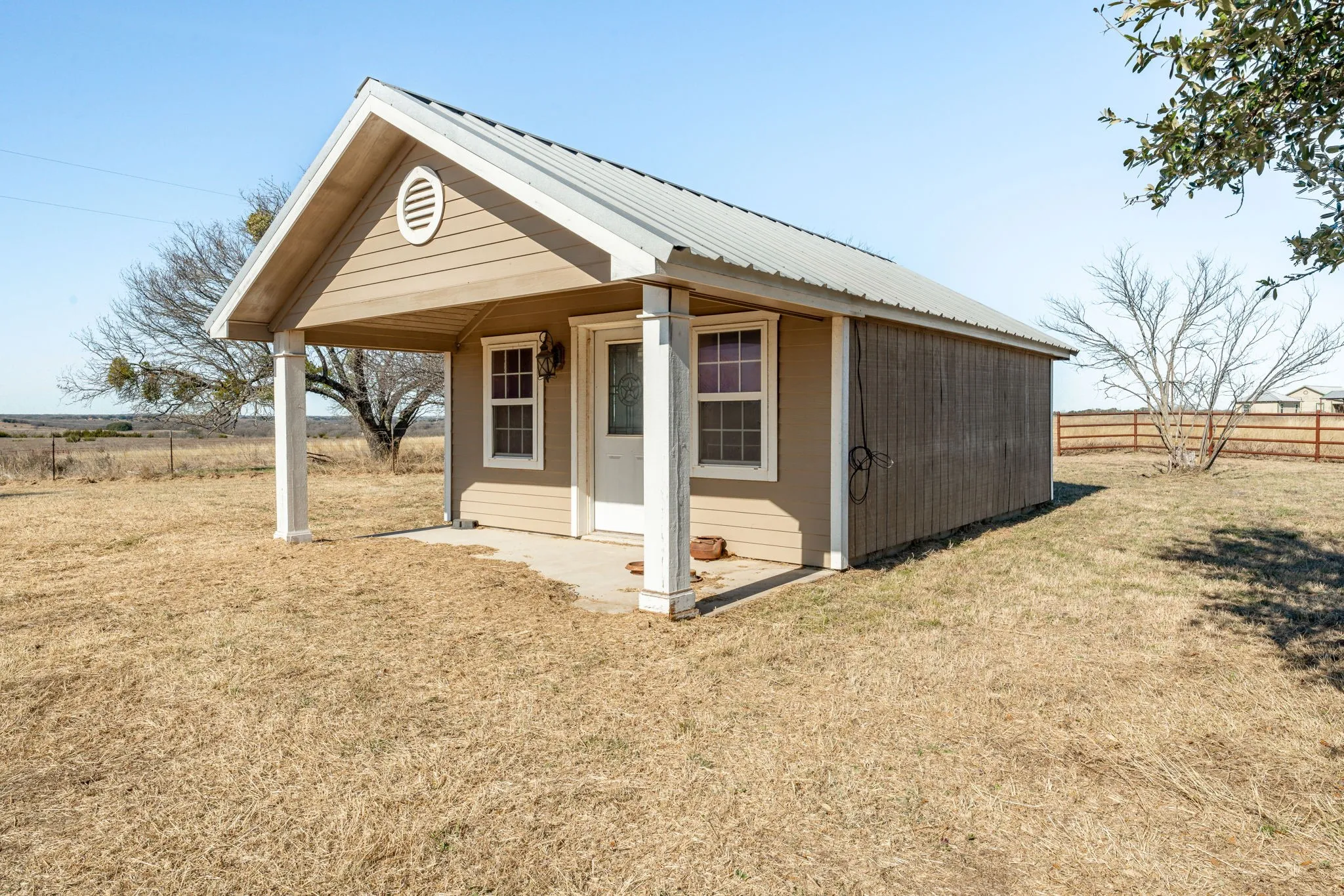 Exterior structure featuring a covered porch with white columns, beige siding, a metal roof, and a single entry door
