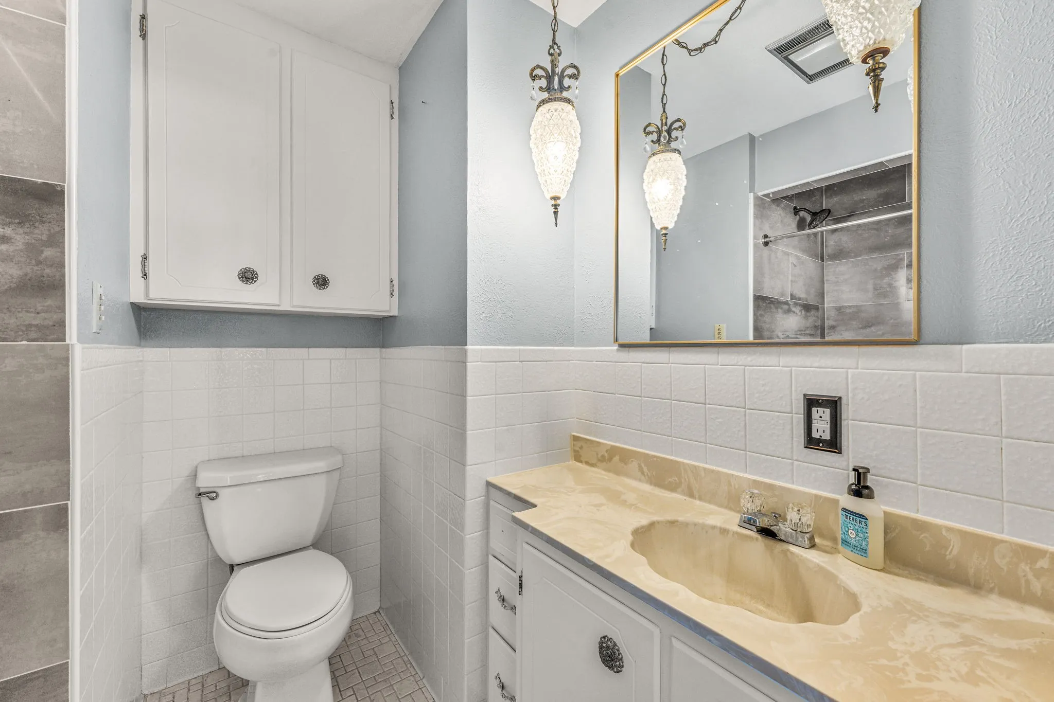 Bathroom featuring a vanity with an integrated sink, white cabinetry, and a gold-framed mirror