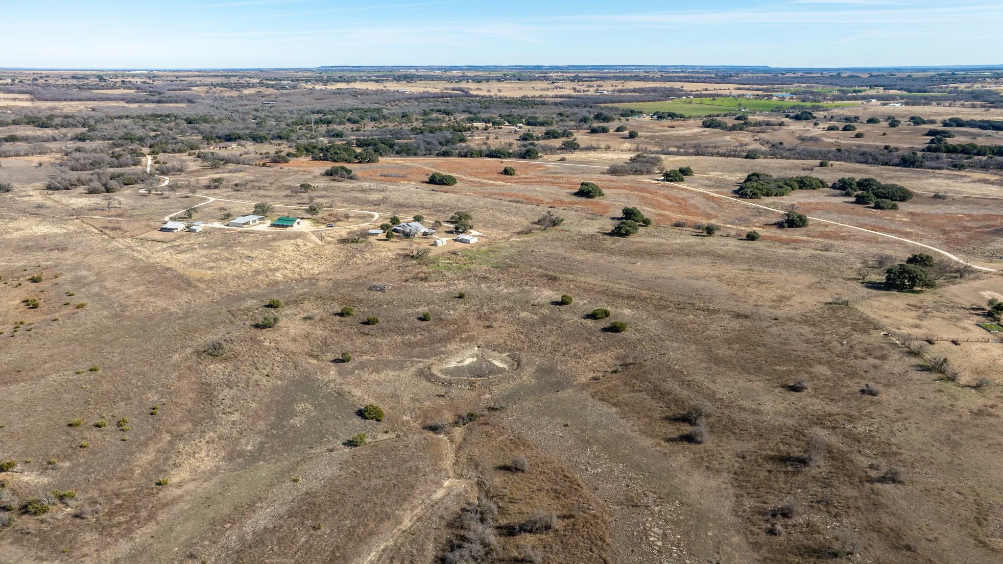 Expansive rural property featuring multiple structures, open fields, scattered mature trees, and unpaved access paths