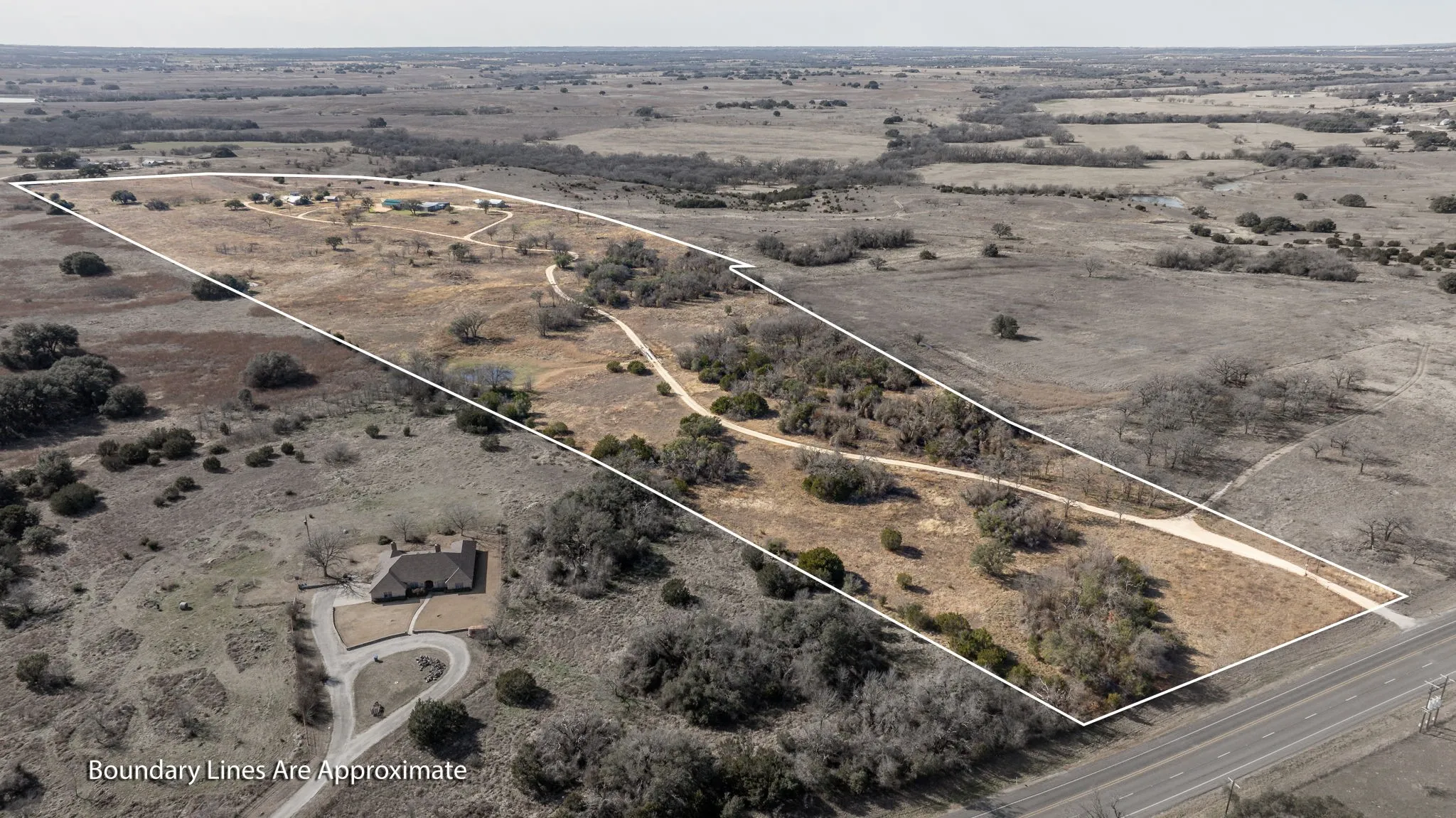 Expansive land parcel featuring multiple structures, a winding driveway, and direct road frontage