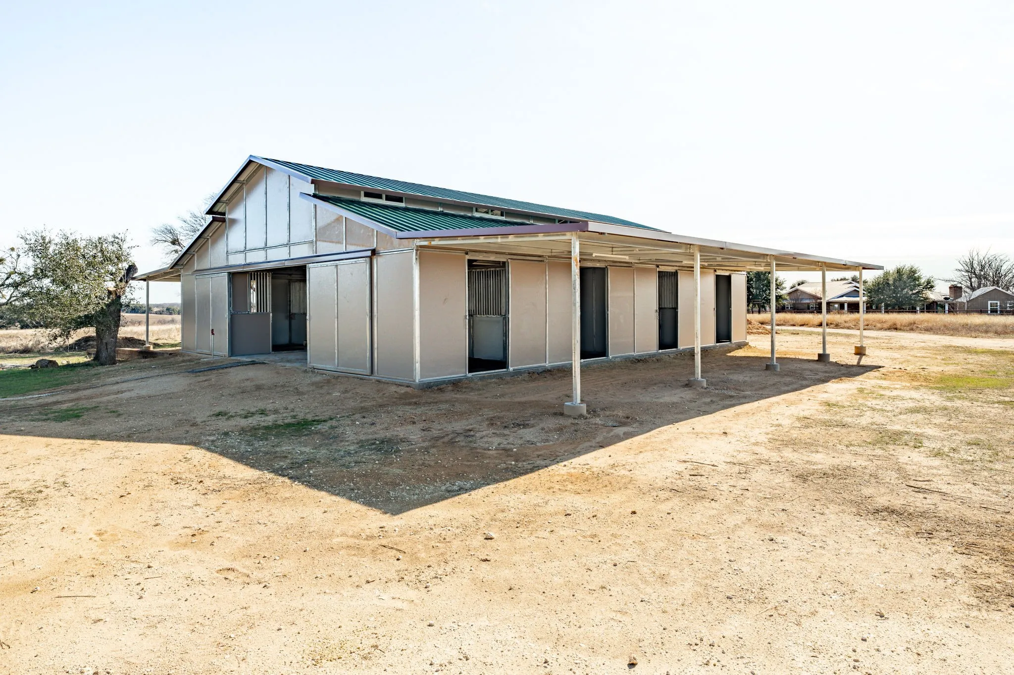 Barn-style structure featuring a green metal roof, light-colored metal siding, and multiple exterior doors
