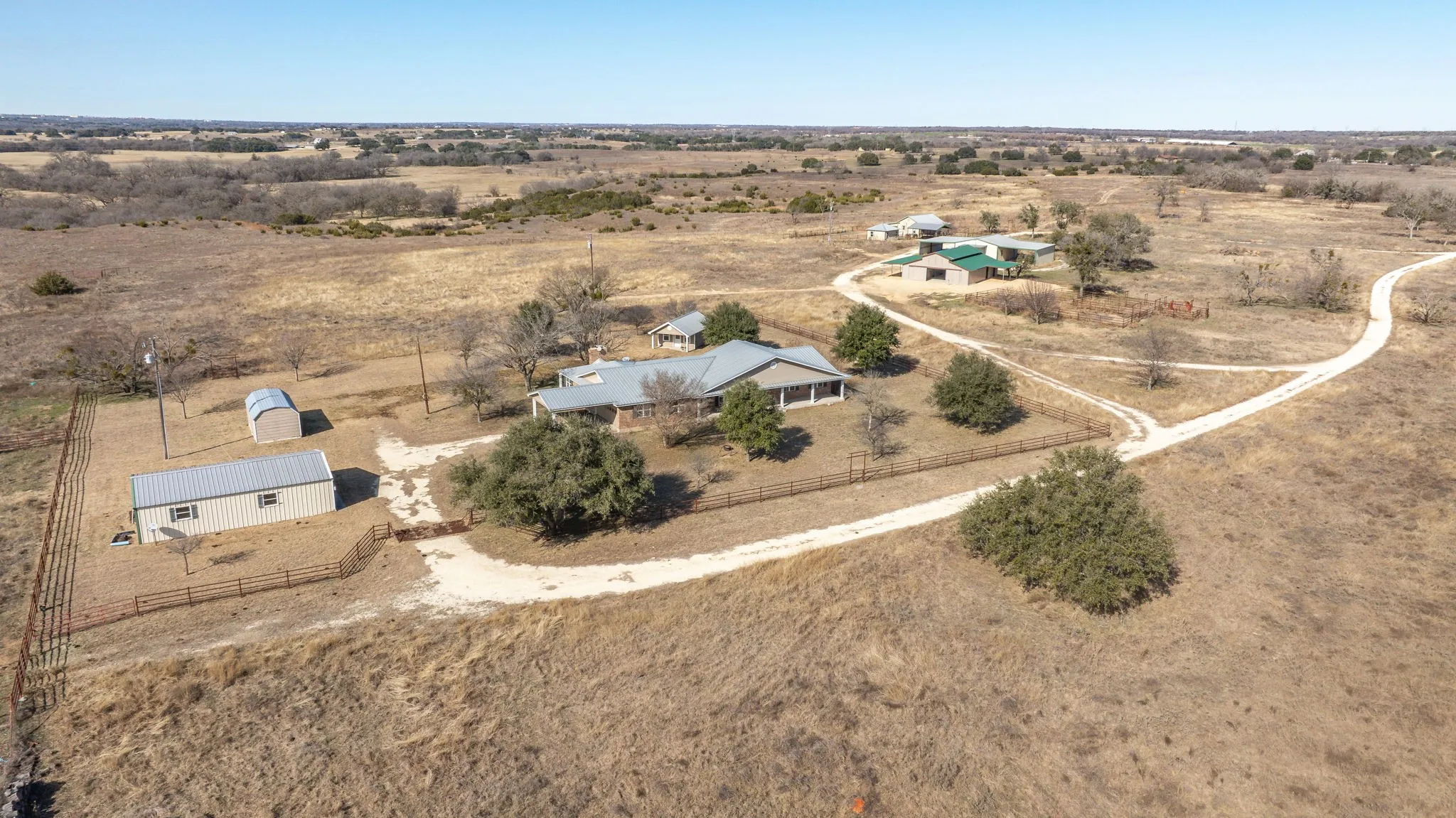 Expansive rural property featuring multiple structures, including a main residence with a covered porch and a metal roof, several outbuildings, and a network of gravel driveways
