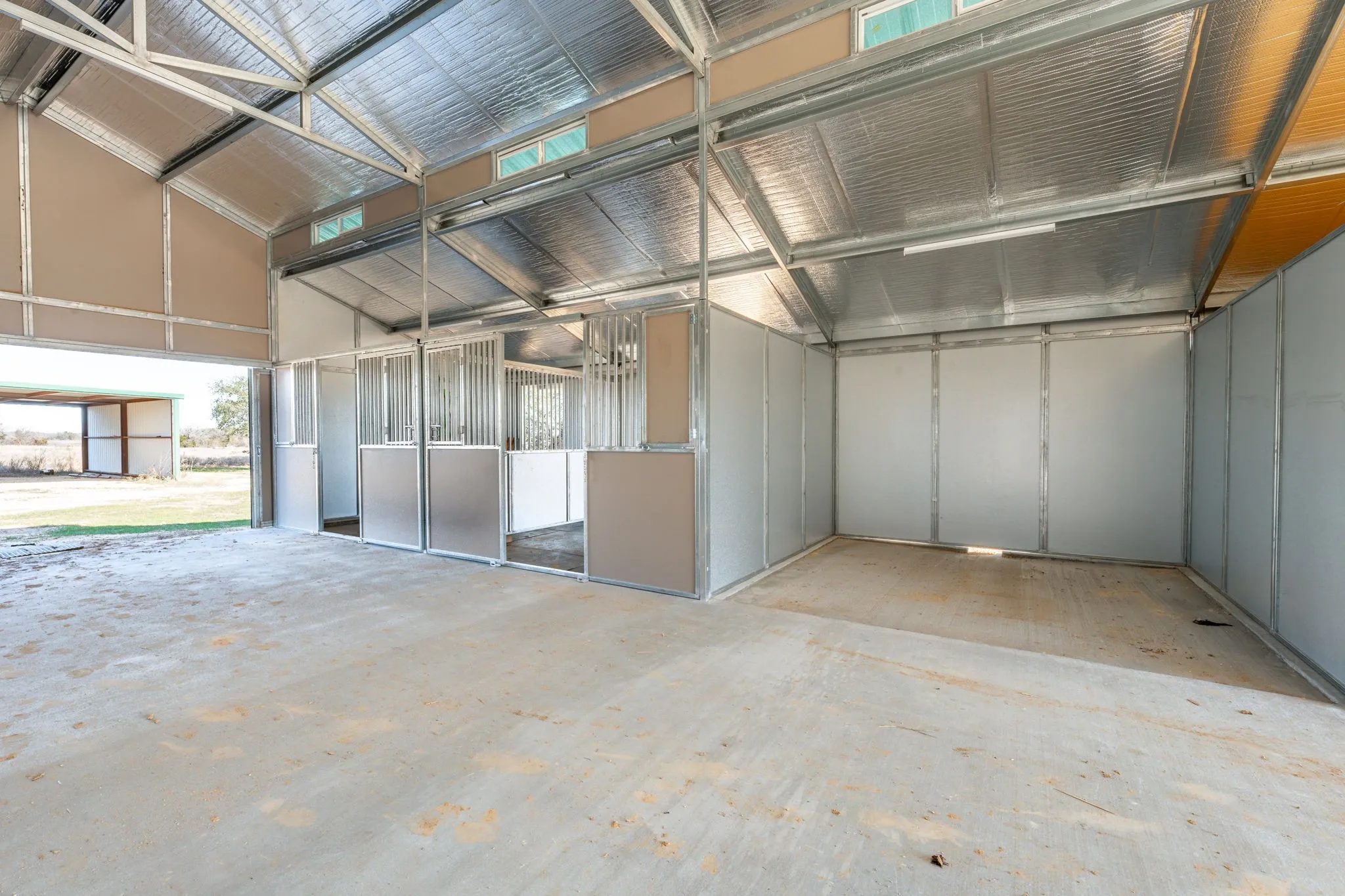 Spacious barn interior featuring multiple stalls with metal grates and solid lower panels