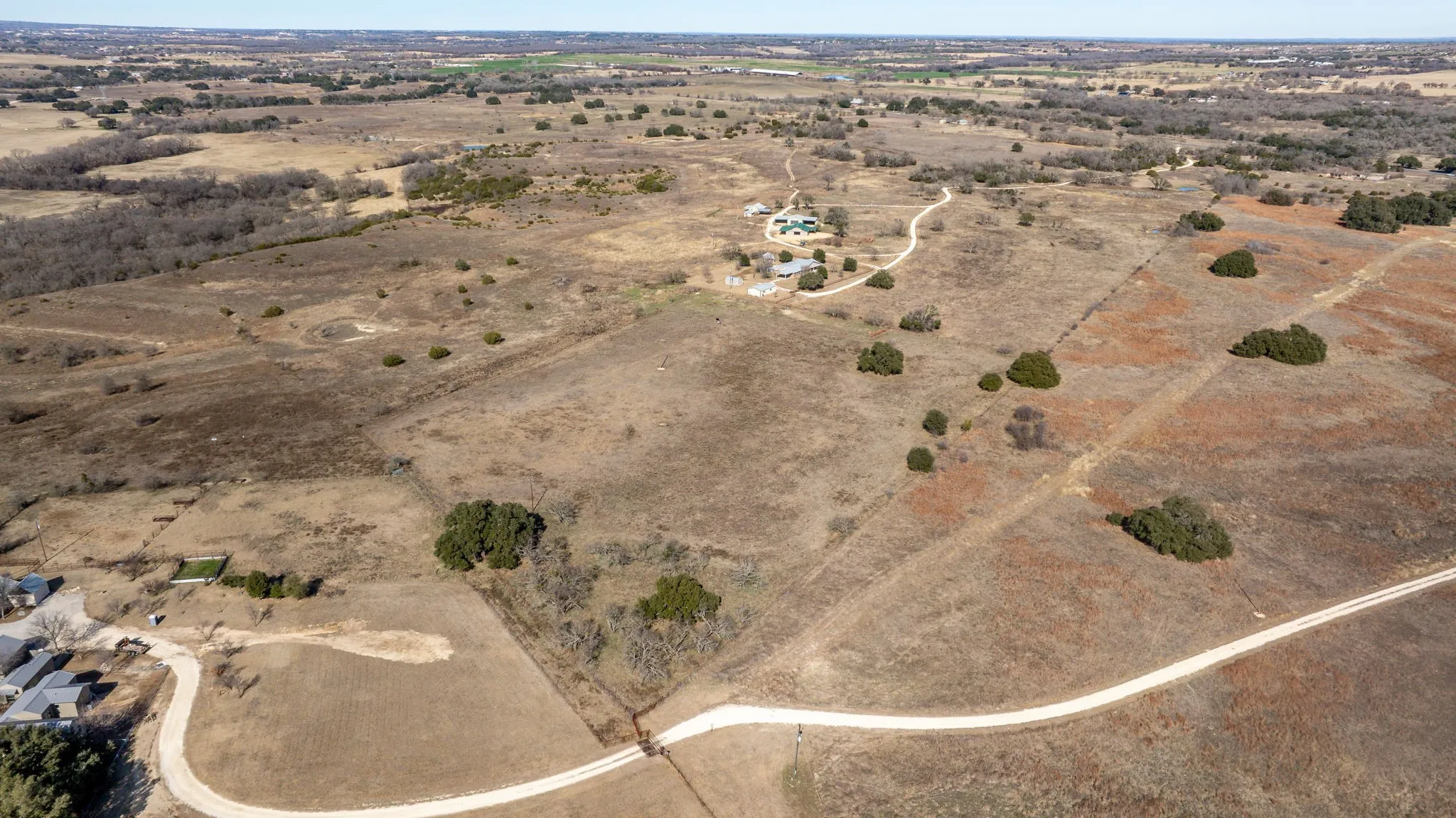 Expansive rural landscape featuring a winding dirt road, scattered trees, and a distant building cluster