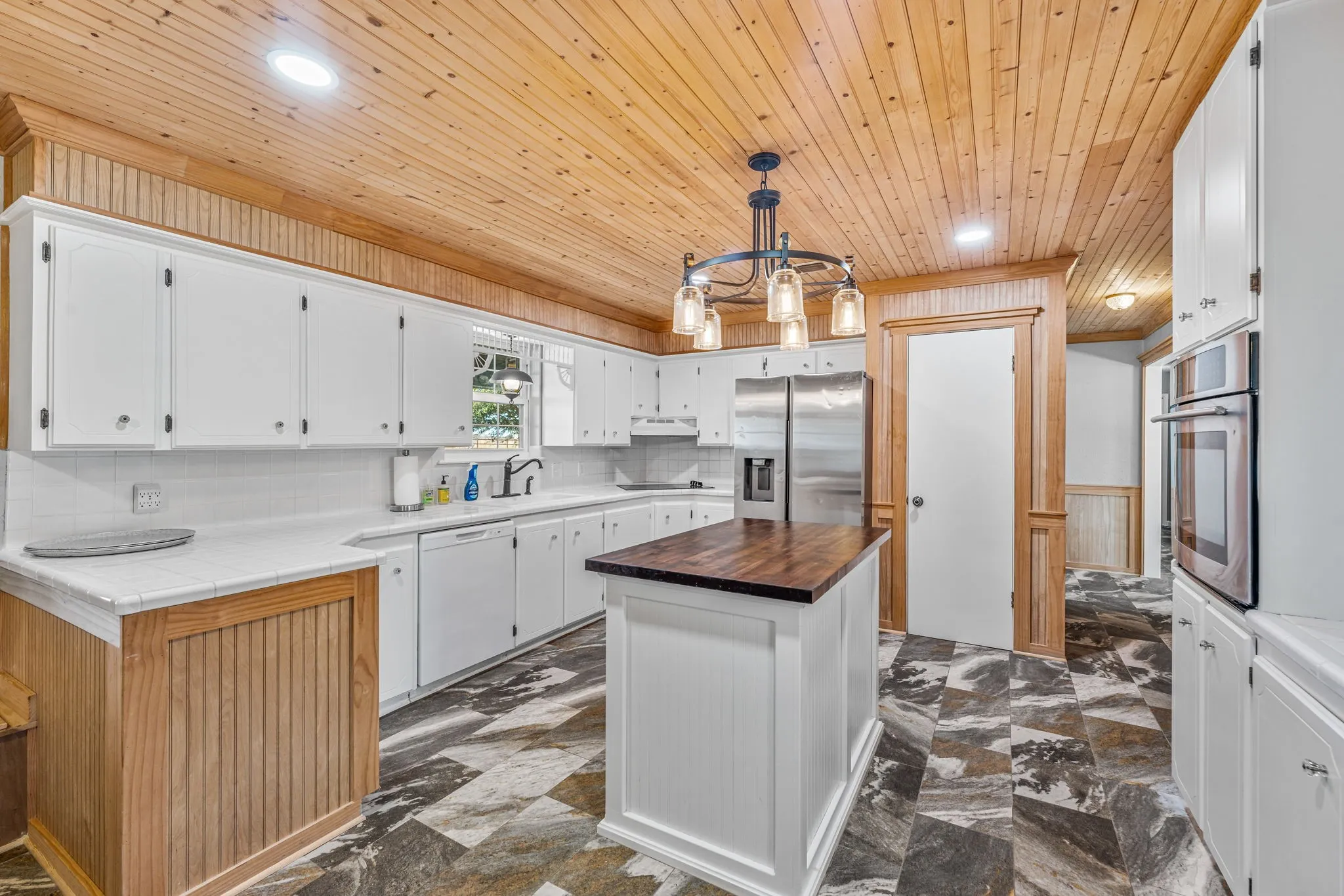 Kitchen featuring a central island with a wood-finish countertop, white cabinetry, integrated stainless steel appliances, a tile backsplash, and wood-paneled ceiling