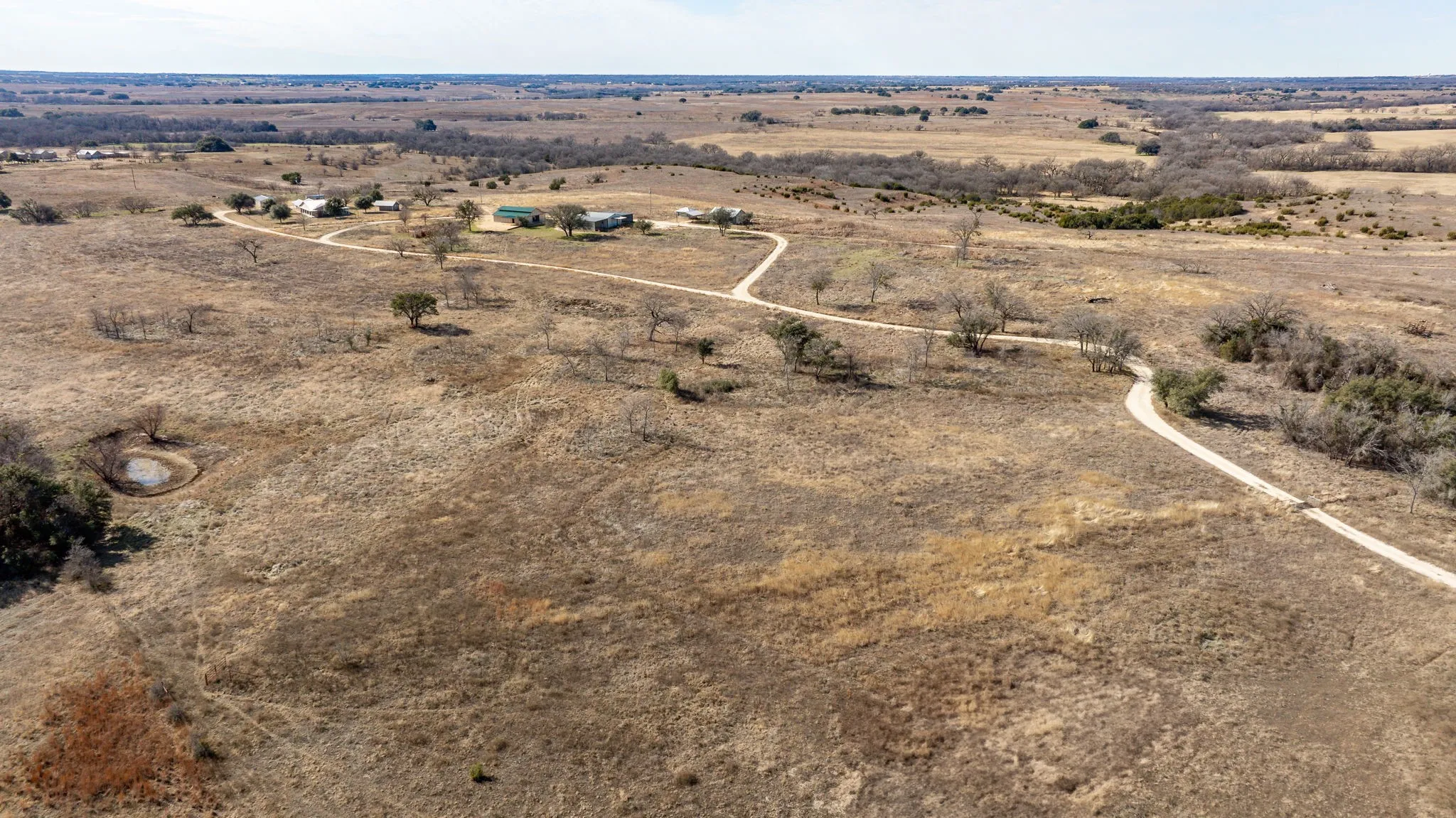 Expansive rural landscape featuring a winding gravel driveway, scattered mature trees, and a visible pond