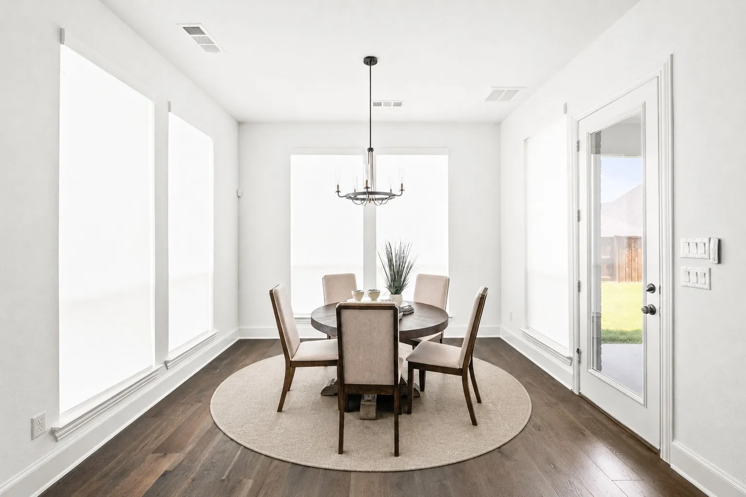 Dining area featuring wood-finish flooring, white baseboards, a full-light glass door, and multiple windows with roller shades