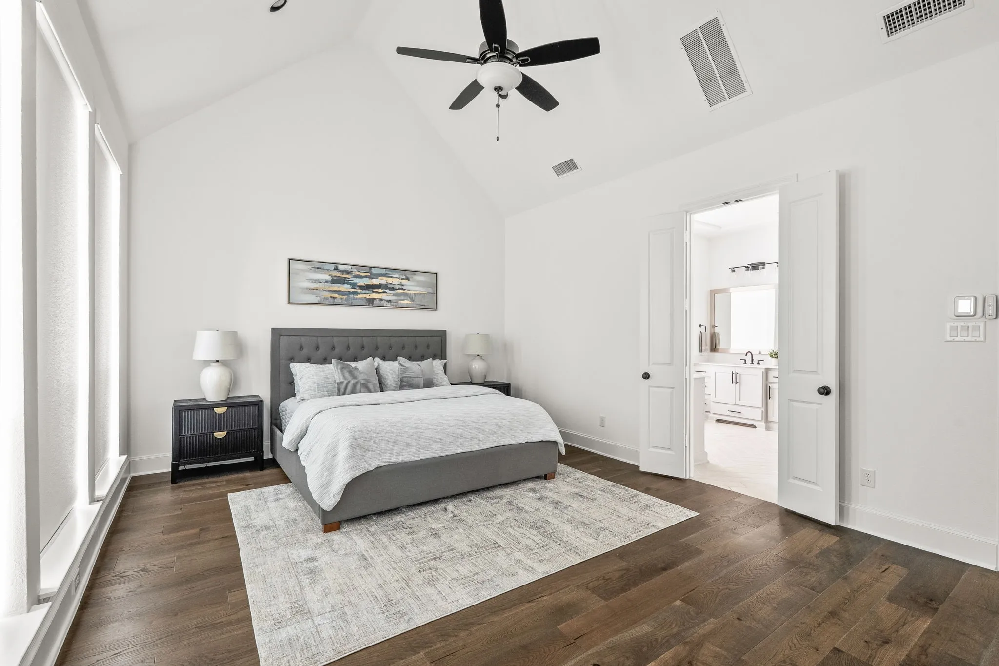 Vaulted ceiling bedroom featuring wood-finish flooring, a ceiling fan, and large windows with roller shades
