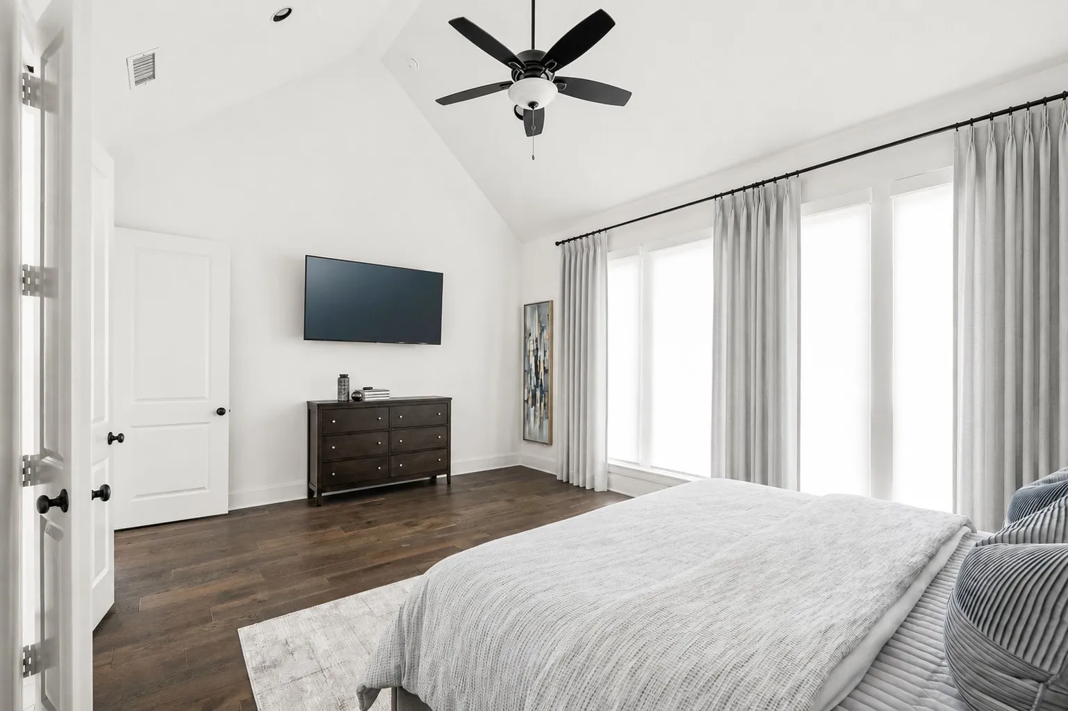 Vaulted ceilings featuring a ceiling fan, dark wood-finish flooring, and multiple windows with drapery