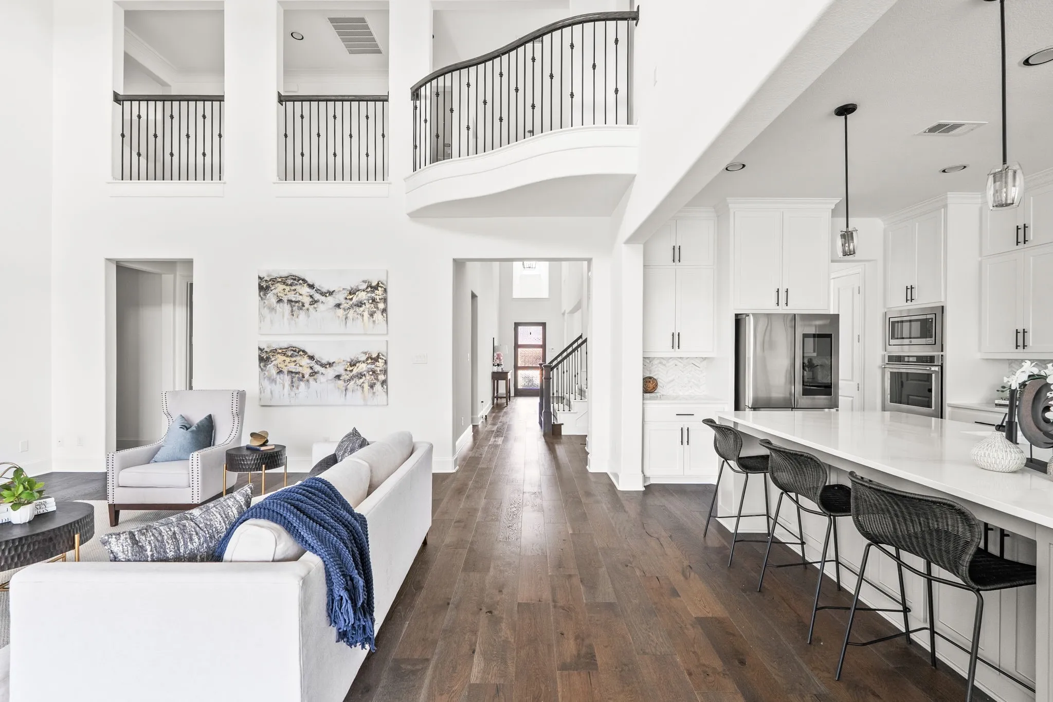 Open-concept living space featuring wood-finish flooring, a two-story ceiling, and a kitchen with white cabinetry and an expansive island