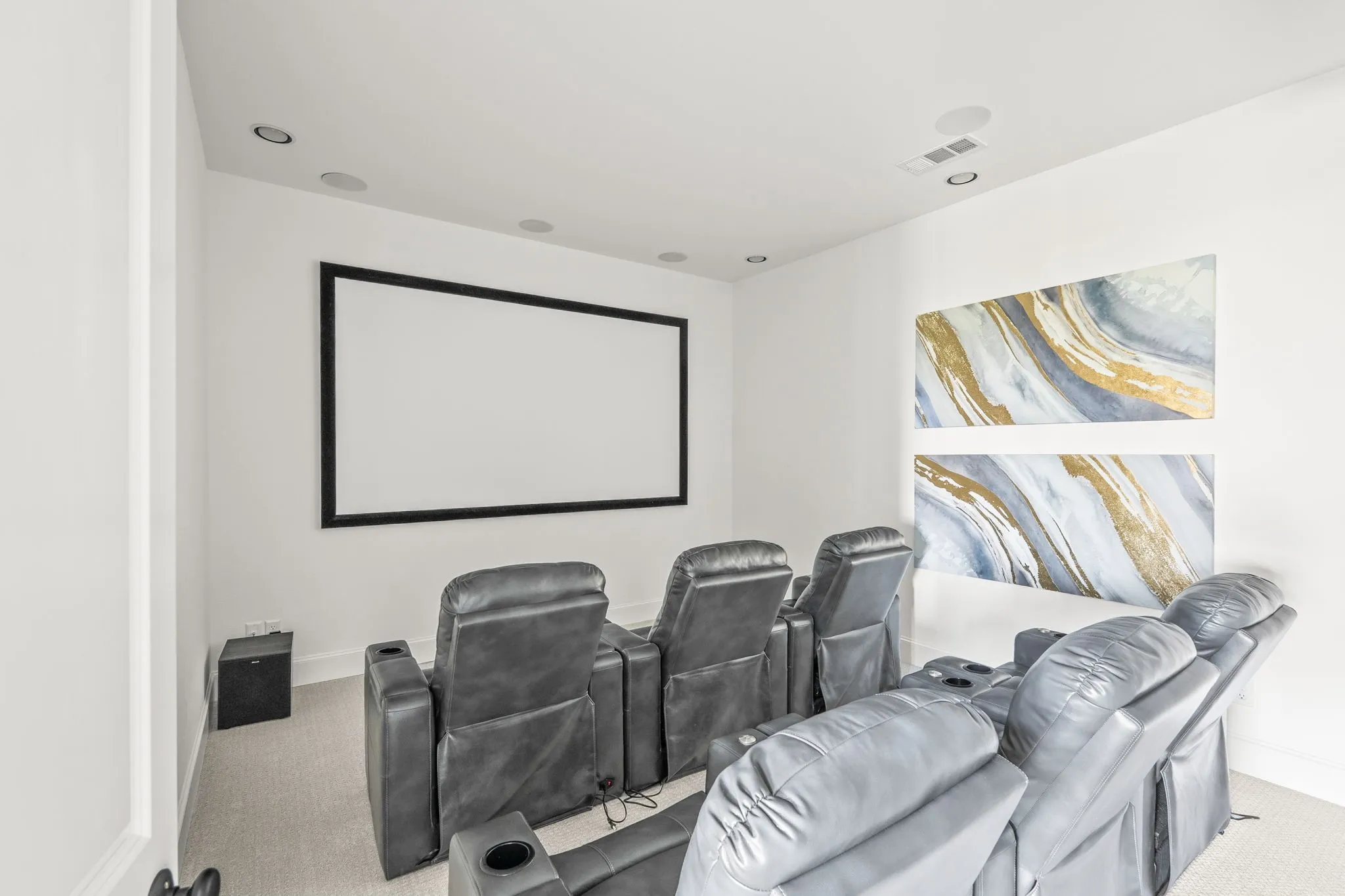 Dedicated media room featuring a large projection screen, recessed lighting, and integrated ceiling speakers