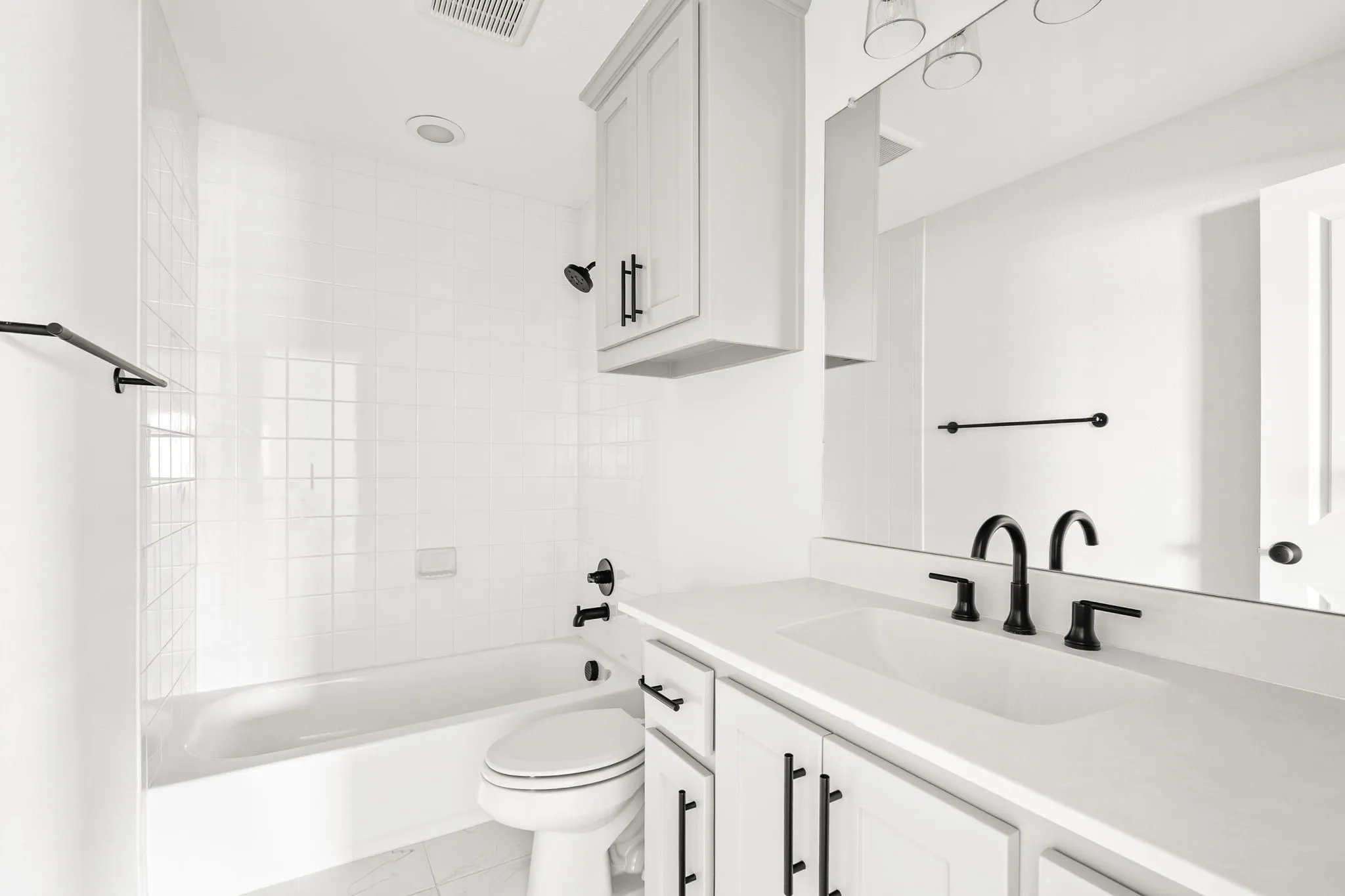 Bathroom featuring a white subway tile tub surround, white vanity with integrated sink, matte black fixtures, and white shaker-style cabinetry with black hardware