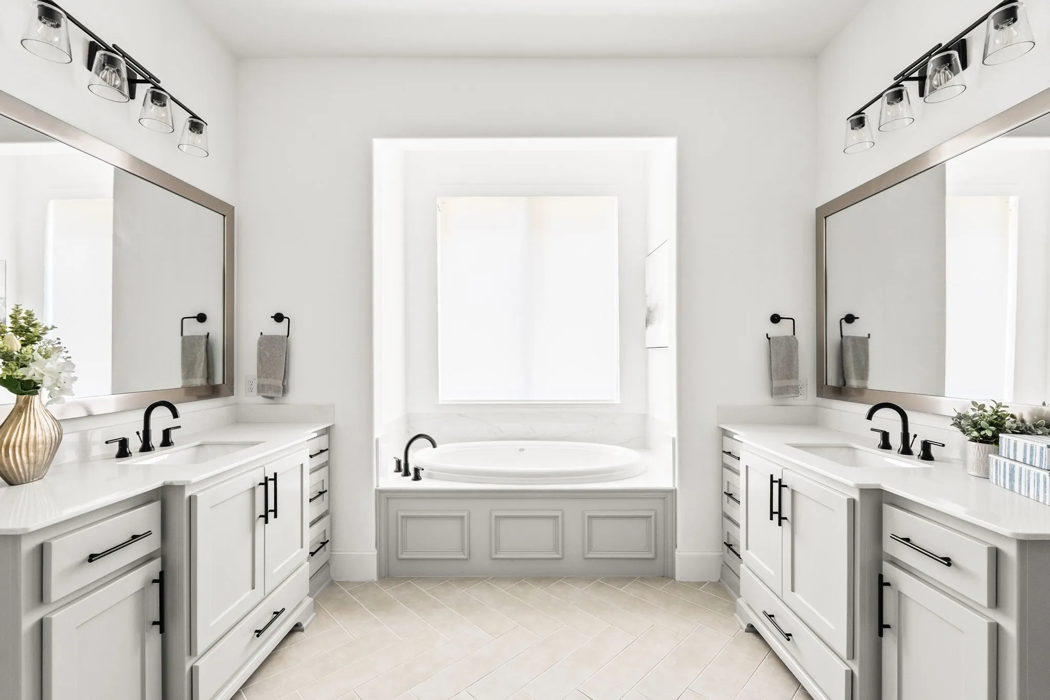 Dual vanity bathroom featuring a built-in soaking tub, white cabinetry, quartz countertops, and matte black fixtures