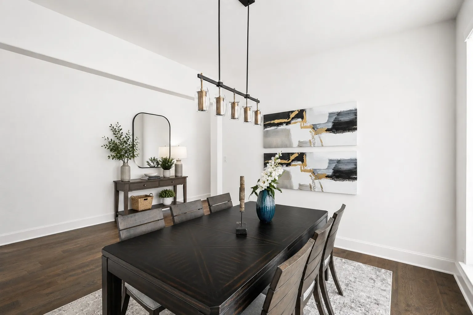 Spacious dining area featuring wood-finish flooring, crisp white walls, and a contemporary linear chandelier with cylindrical glass shades