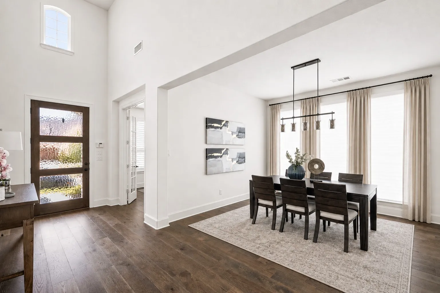 Foyer and dining area featuring wood-finish flooring, a contemporary linear chandelier, tall ceilings, and a wood entry door with frosted glass panels