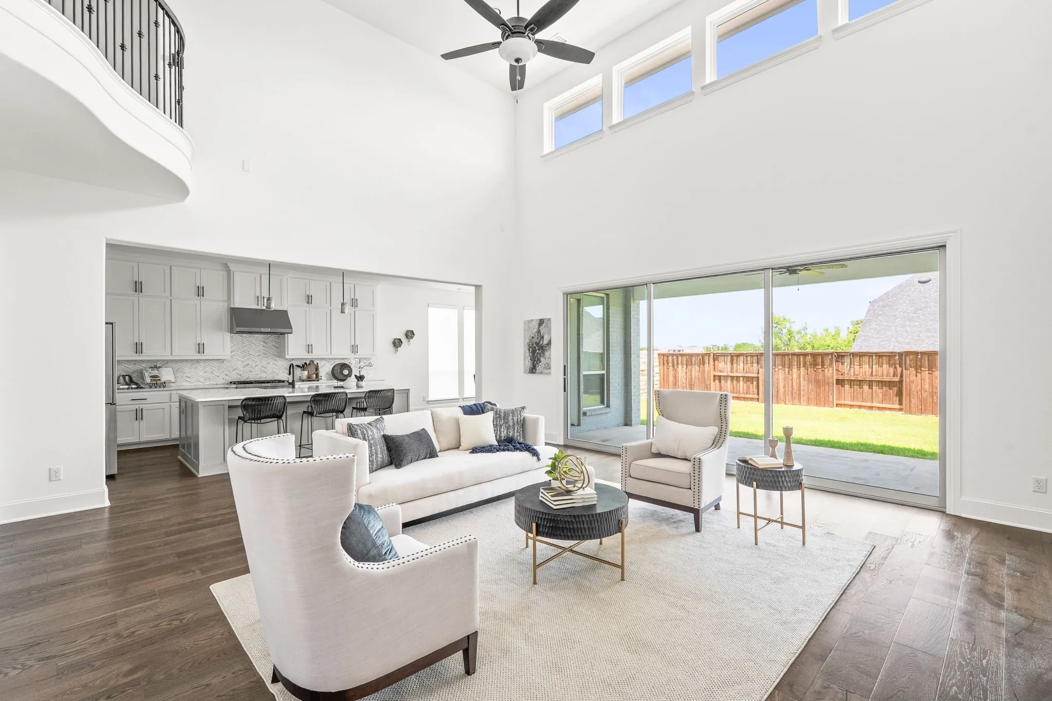 Two-story living area featuring a vaulted ceiling with a ceiling fan, a second-story balcony with wrought iron railing, and wood-finish flooring