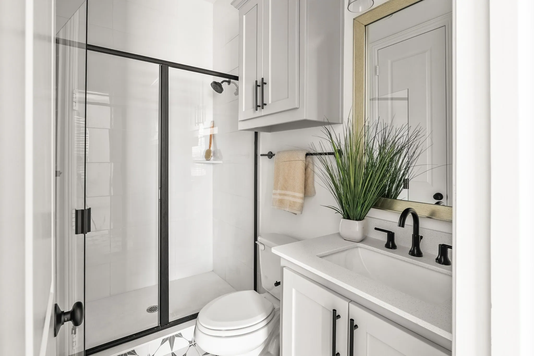 Bathroom featuring a glass-enclosed shower with matte black fixtures, a white vanity with a rectangular sink, a light-colored countertop, and patterned floor tiling
