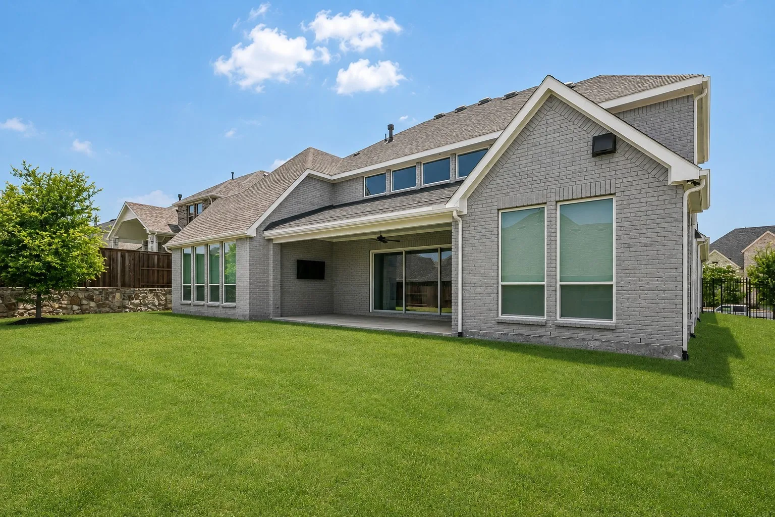 Expansive green lawn, covered patio, gray brick exterior, multiple large windows, and a multi-level roofline