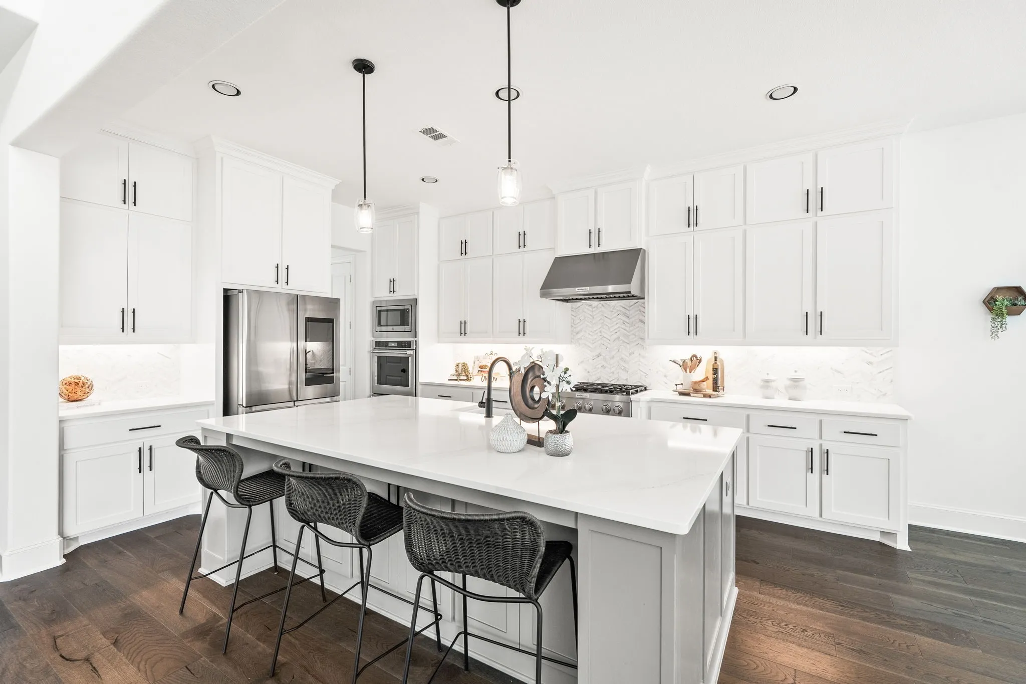 Modern kitchen featuring white cabinetry with dark hardware, stainless steel appliances, a white island with seating, and dark wood-finish flooring