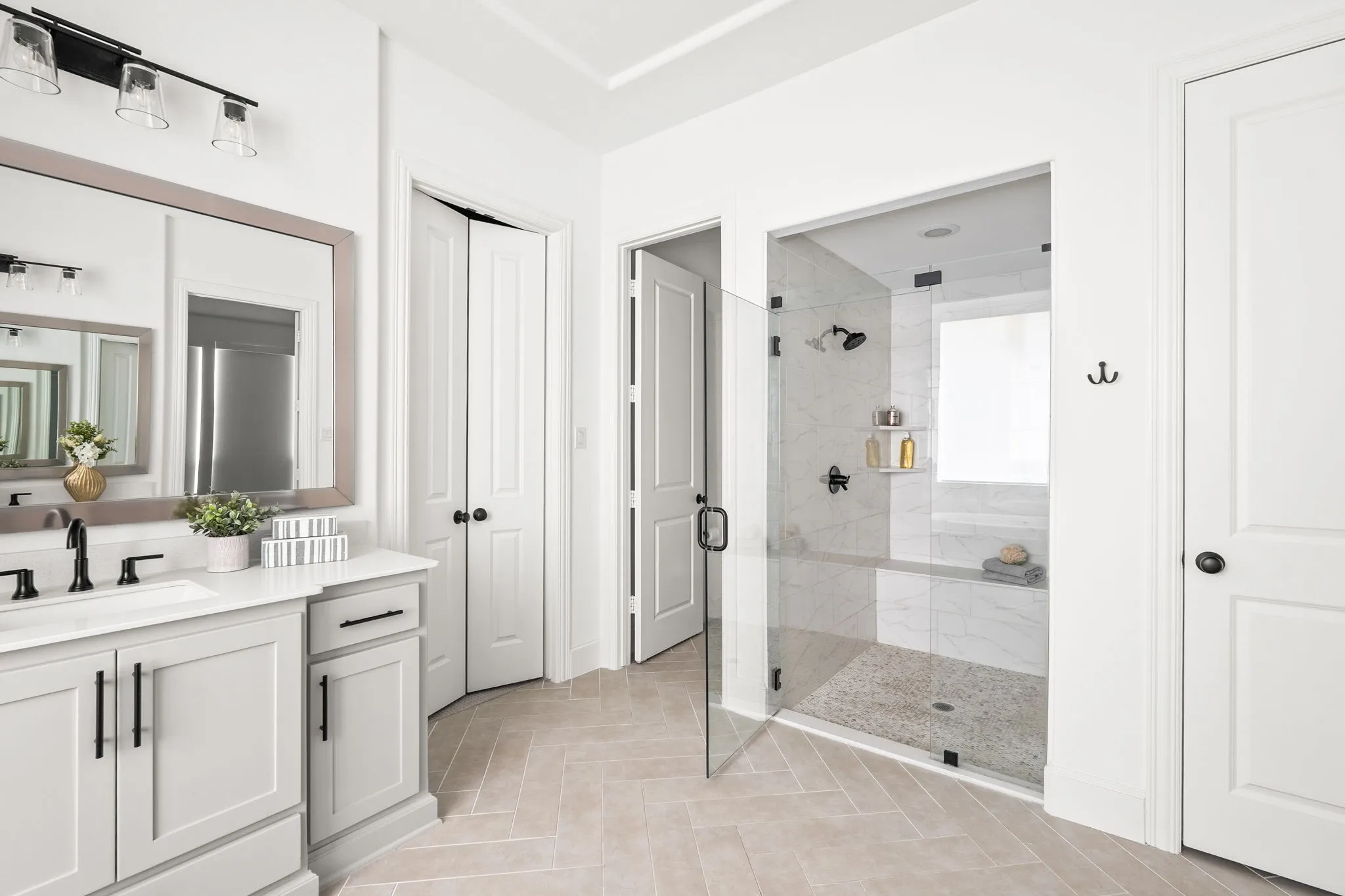 Bathroom featuring a double vanity with light gray cabinetry, a walk-in shower with a glass enclosure, herringbone tile flooring, and matte black fixtures