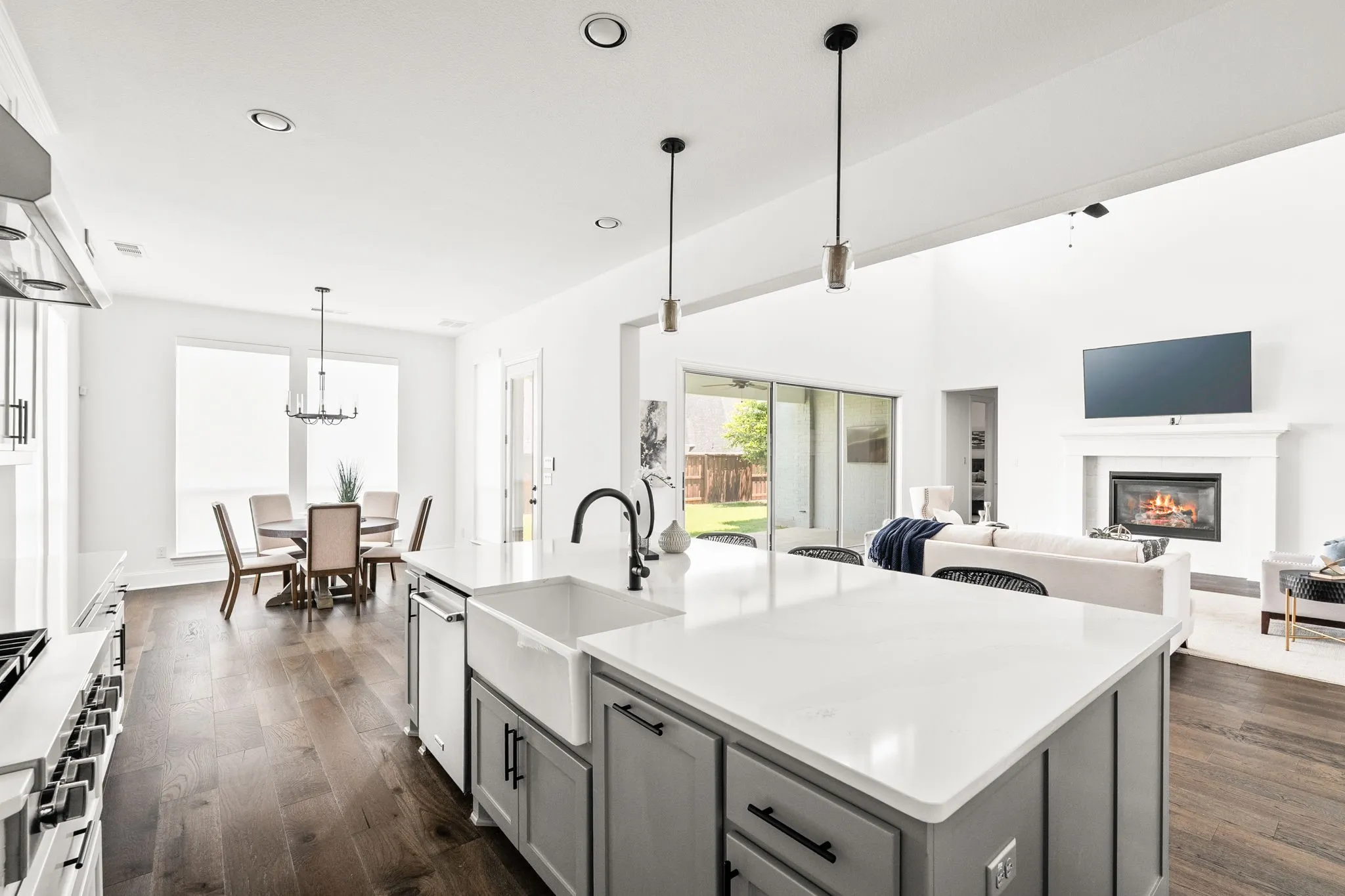 Kitchen island featuring a farmhouse sink and light gray cabinetry, complemented by recessed lighting and pendant fixtures