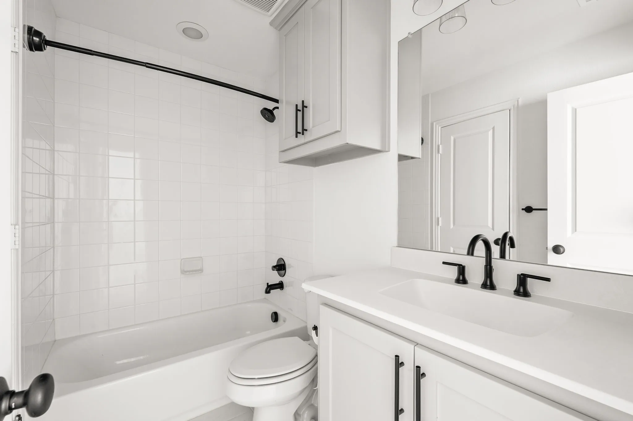 Bathroom featuring a full-size bathtub with subway tile surround, white vanity cabinetry, a solid surface countertop, and black hardware throughout