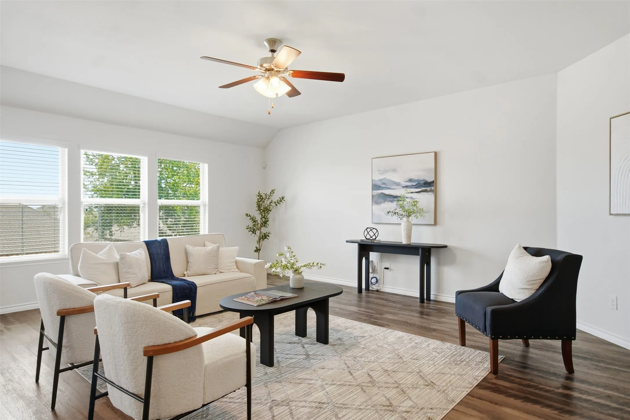 Vaulted ceilings, wood-finish flooring, a ceiling fan with integrated lighting, and multiple windows with blinds