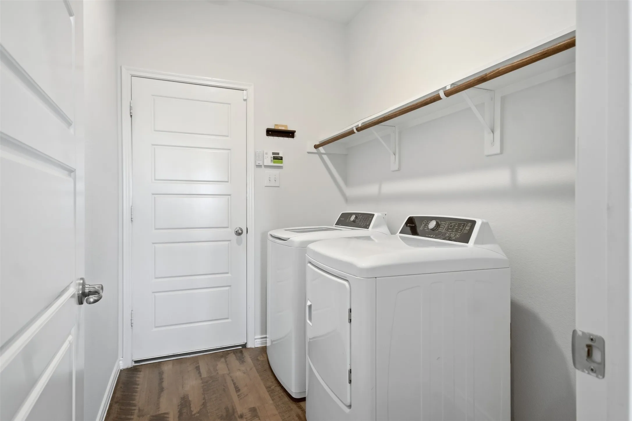 Dedicated laundry area featuring wood-finish flooring, white walls, and a built-in shelving unit with a hanging rod