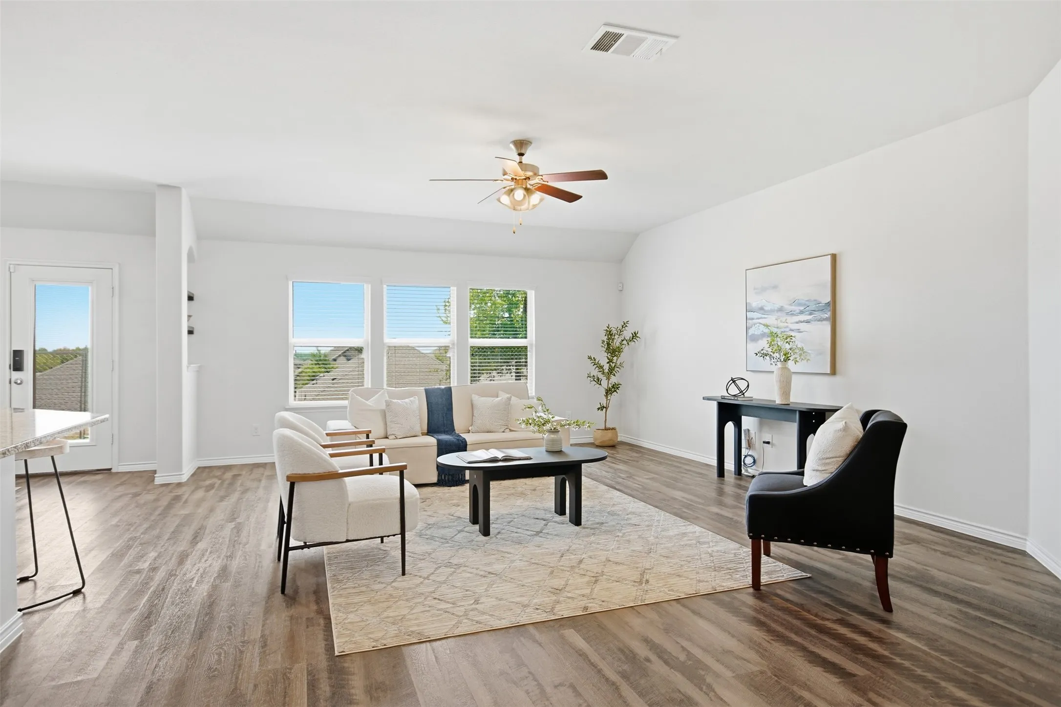 Spacious living area featuring wood-finish flooring, ample natural light from multiple windows, and a ceiling fan