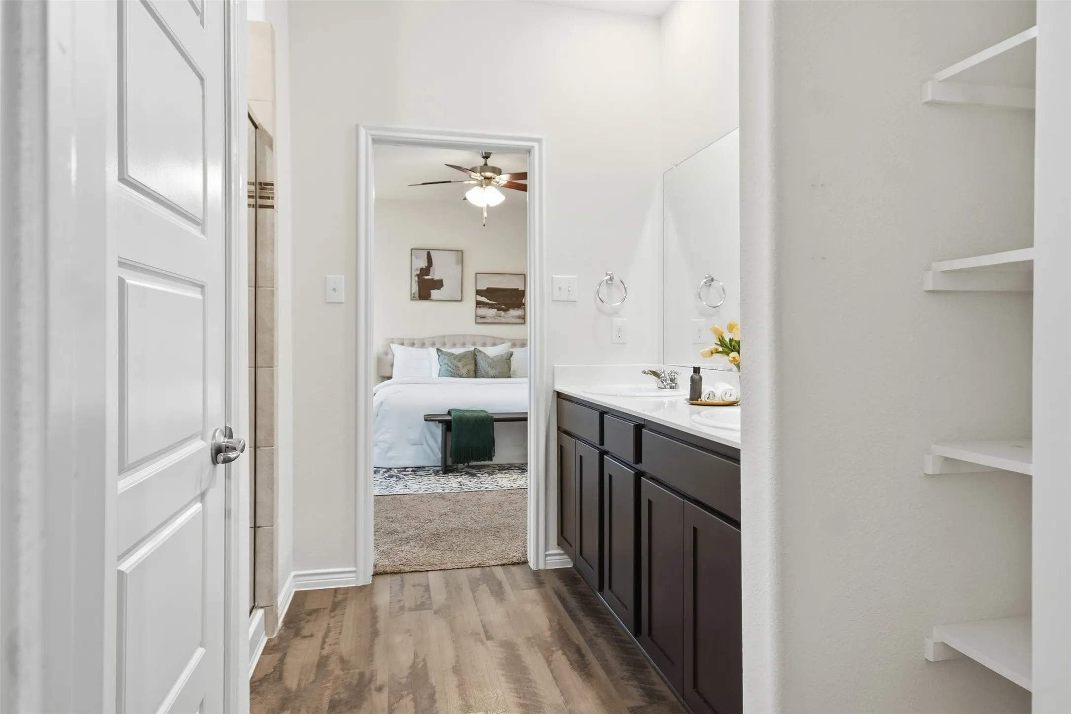 Wood-finish flooring, dark wood-finish vanity with dual sinks, white countertop, and built-in shelving