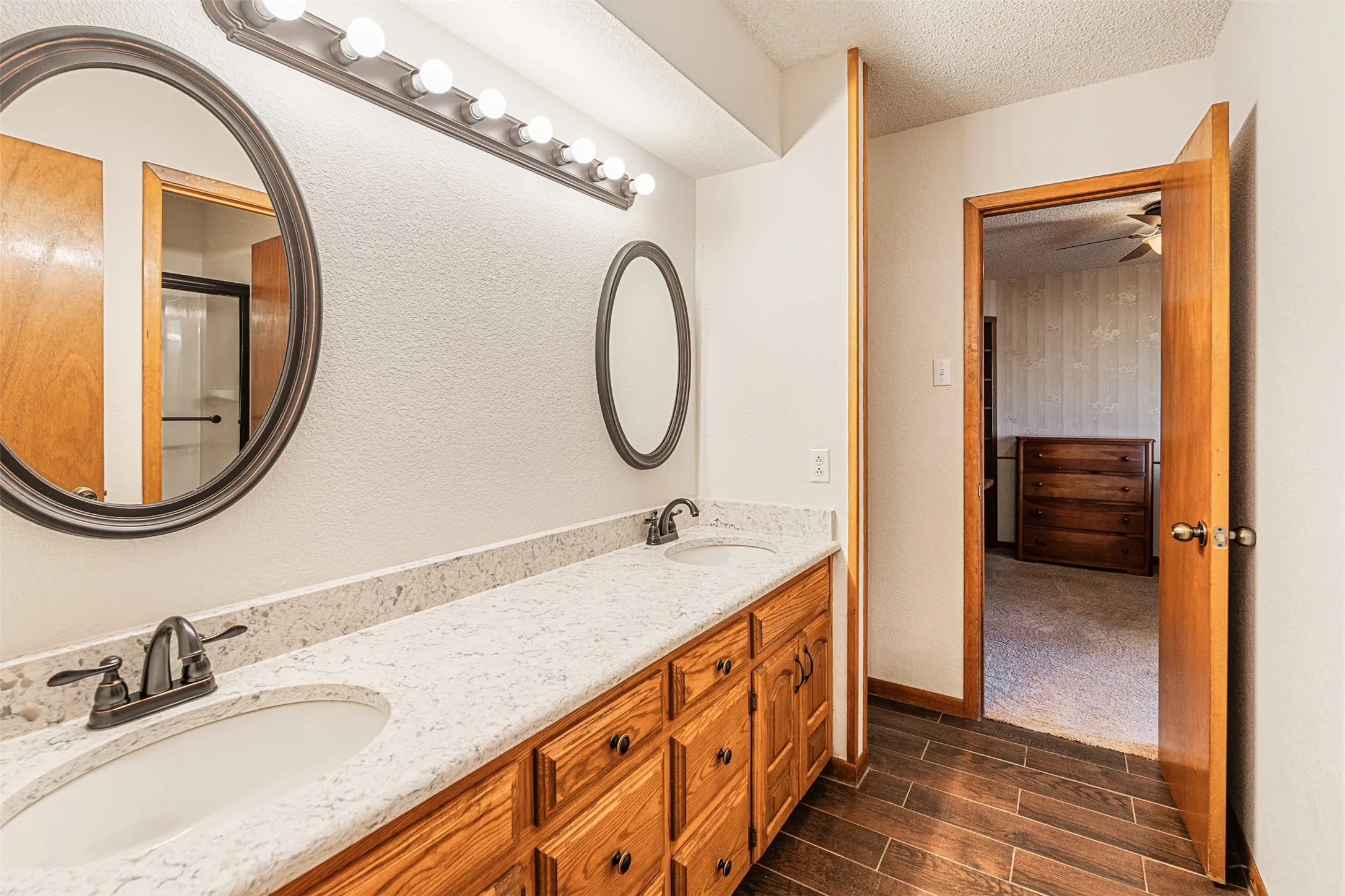 Full bath with a textured ceiling, wood finish floors, a shower with door, and double vanity